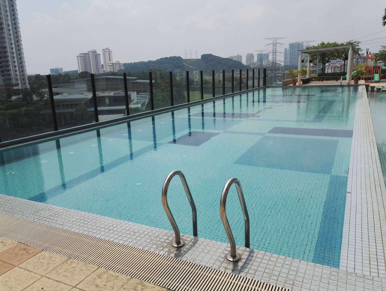 Serviced Residence @ Pelangi Damansara Sentral: Rooftop infinity-edge swimming pool with stainless steel ladder rails, glass safety railing, and city skyline view in the background