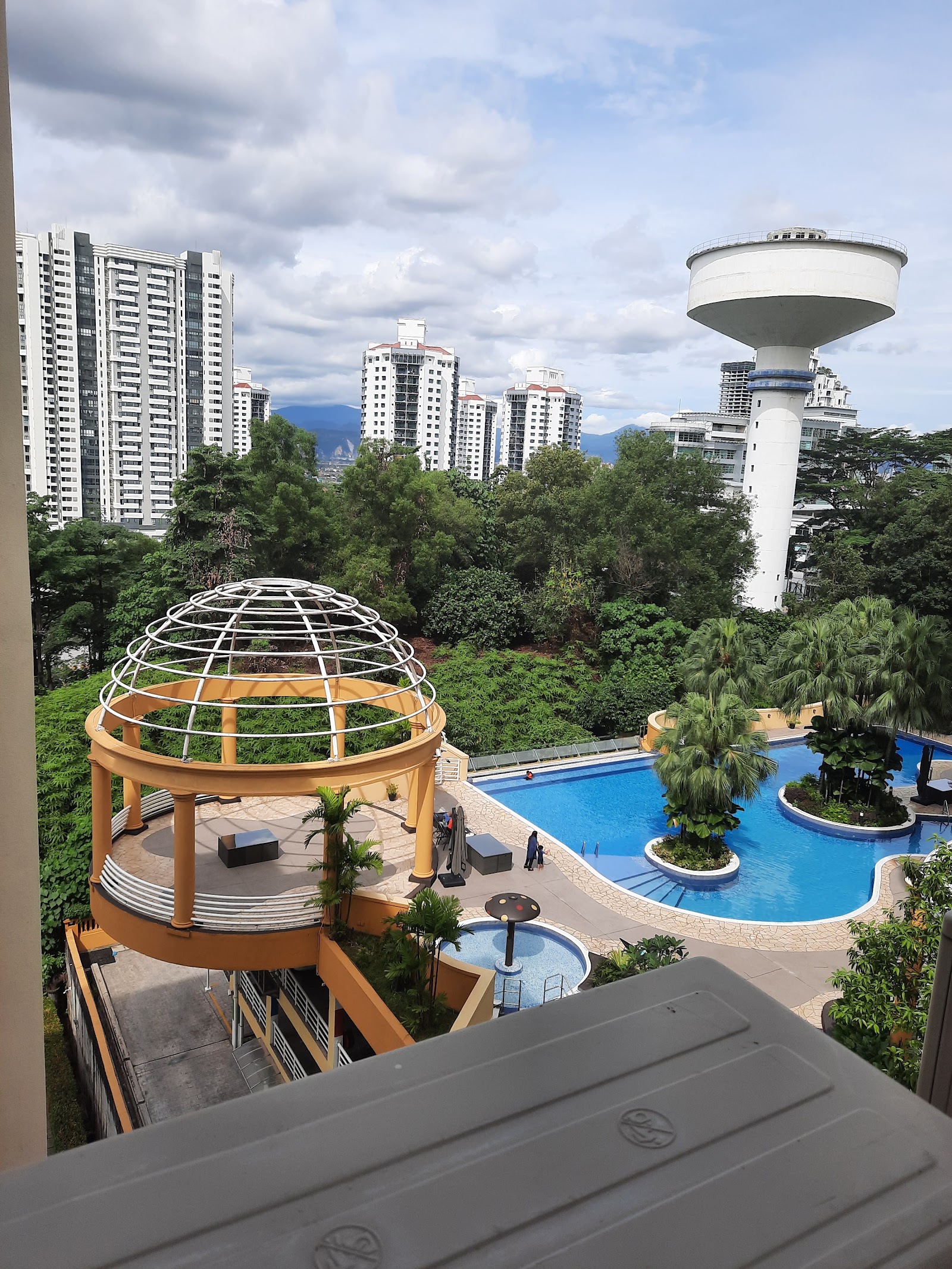 La Grande Kiara: View from a balcony overlooking a resort-style swimming pool with a dome-topped gazebo structure, surrounded by trees and high-rise towers in the background