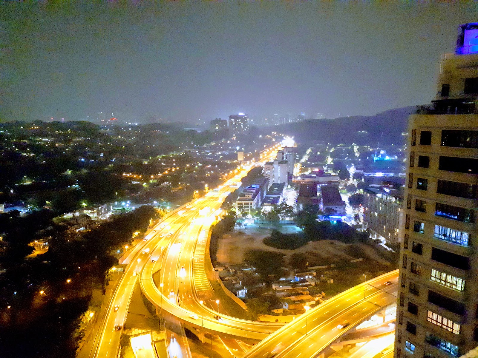 i-Zen @ Kiara 2: Night-time aerial view from a high-rise unit showing a curving illuminated highway interchange, city lights, and surrounding buildings