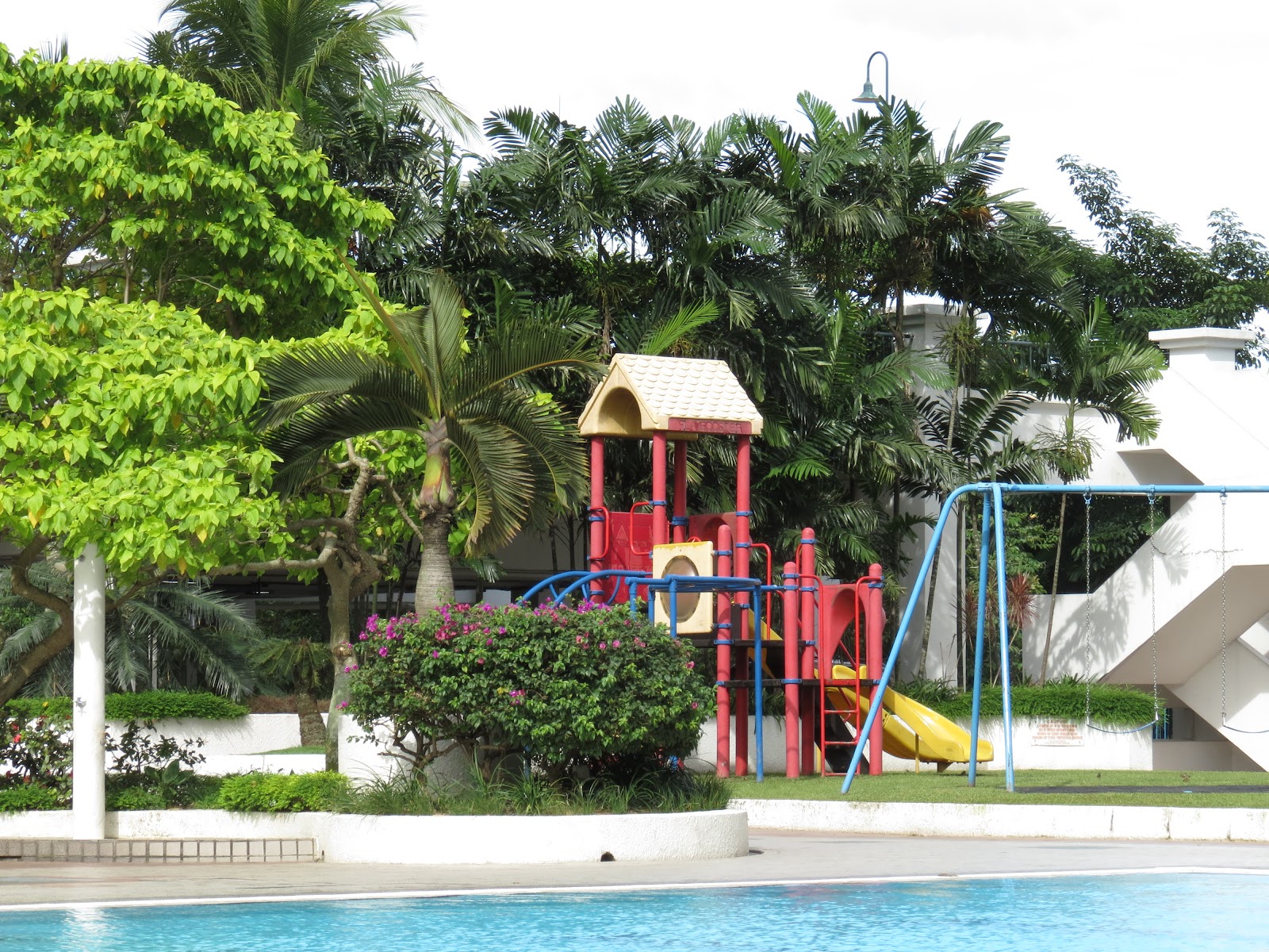 Desa Kiara: A children's playground with slides and swings surrounded by trees, next to a swimming pool