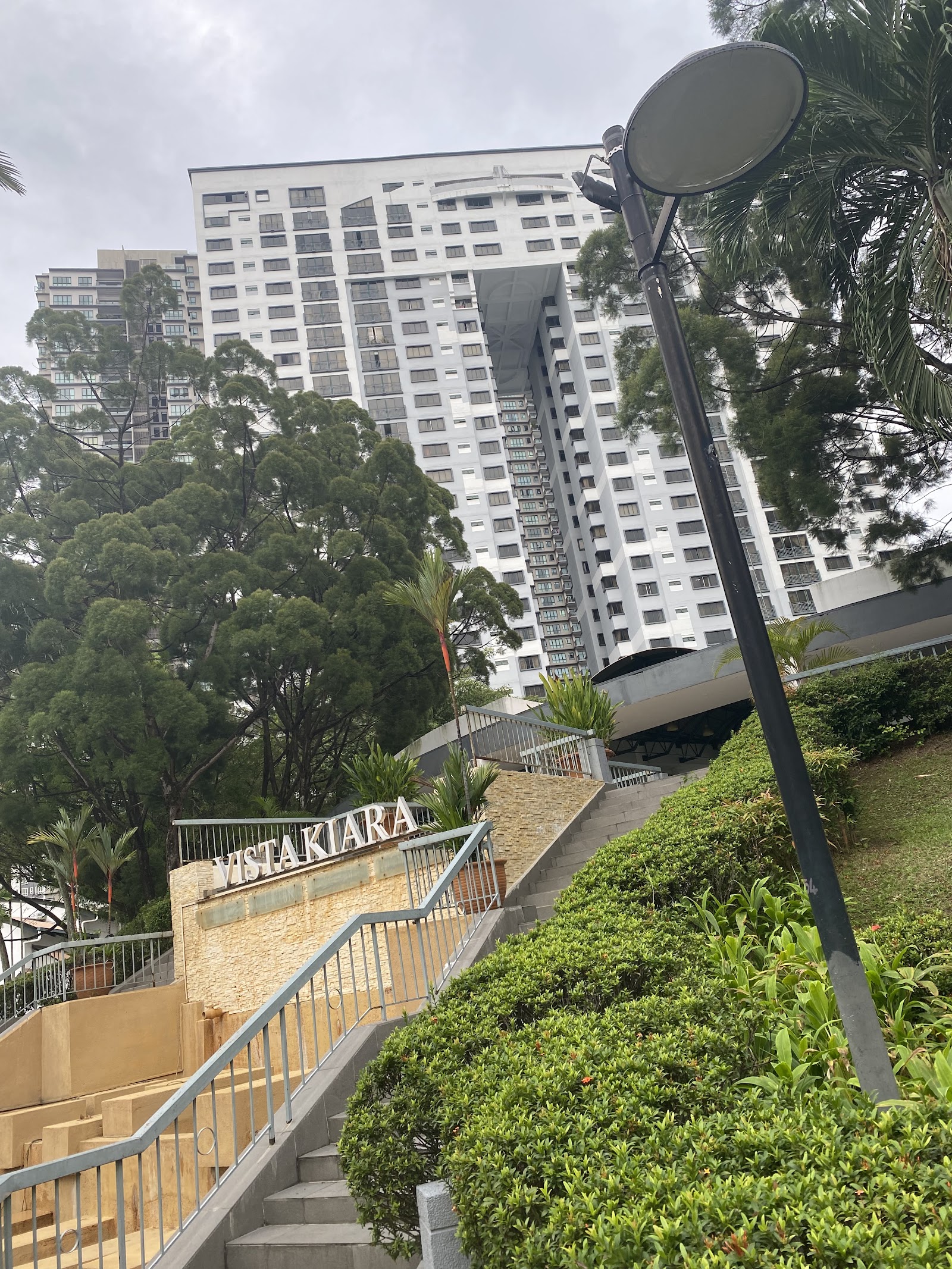 Vista Kiara: A high-rise residential tower called Vista Kiara seen from ground level, with a staircase, entrance sign, trees and landscaping in the foreground