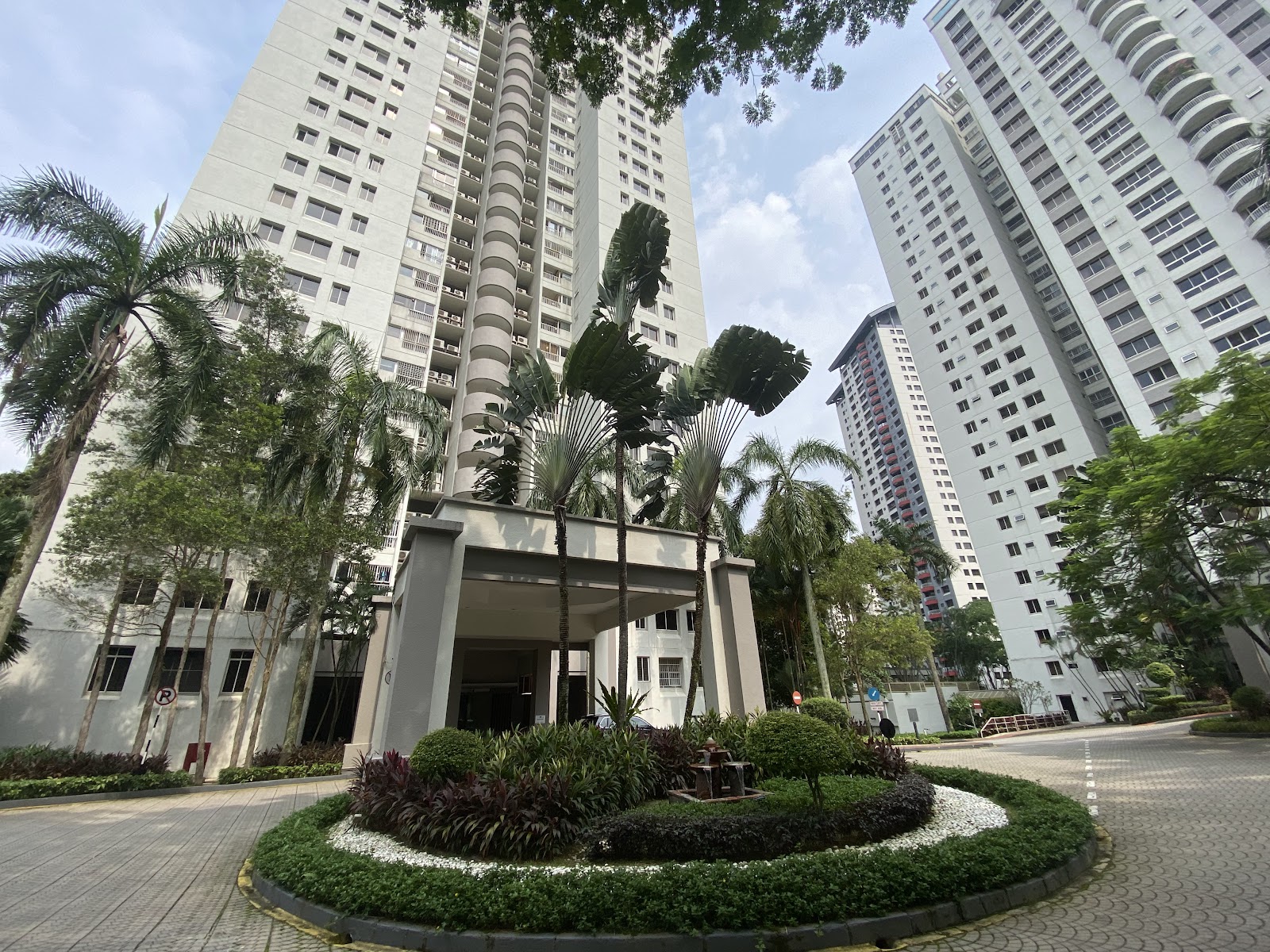 Mont Kiara Pelangi: View of high-rise condominium towers with a landscaped entrance driveway and roundabout garden, surrounded by palm trees