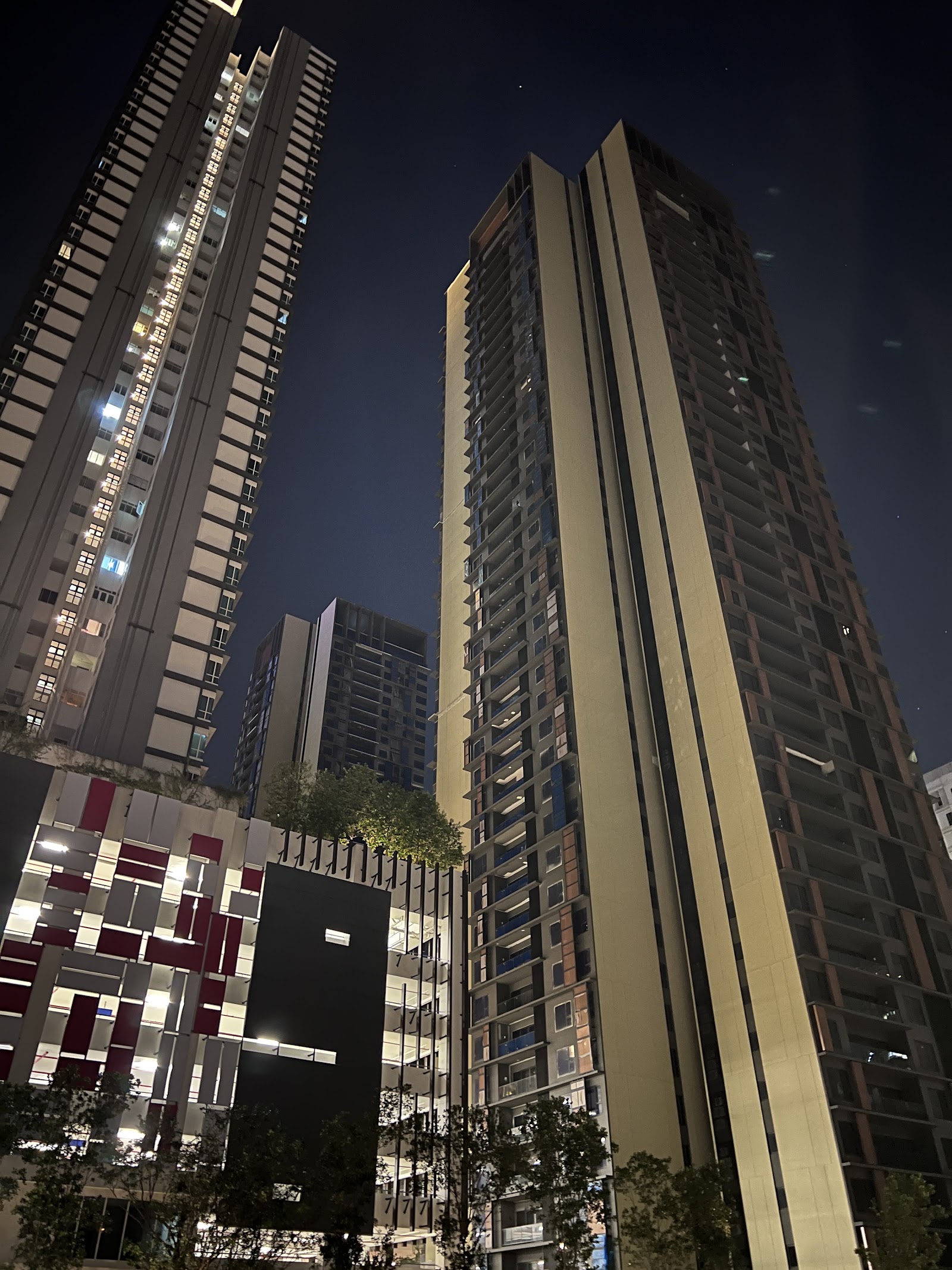Allevia: Night-time view of several tall residential towers, including a beige-gold high-rise, seen from ground level looking up