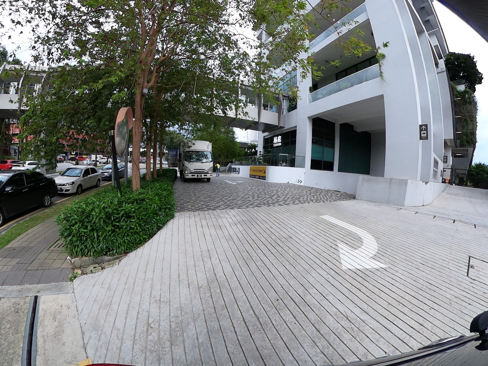 The Greens: Street-level view of a modern building exterior with a delivery truck, parked cars, and trees along a driveway