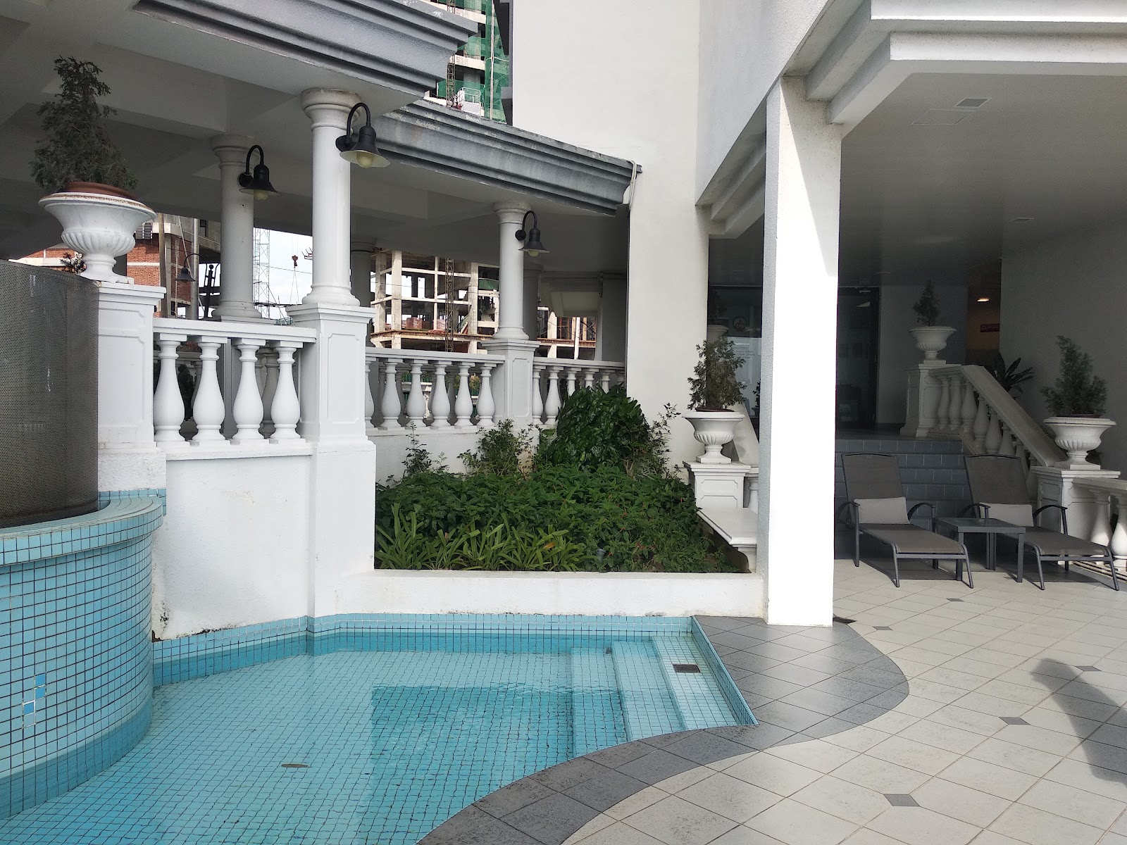 Contessa: Poolside patio area with lounge chairs, balustrades, planters, and greenery under a covered walkway