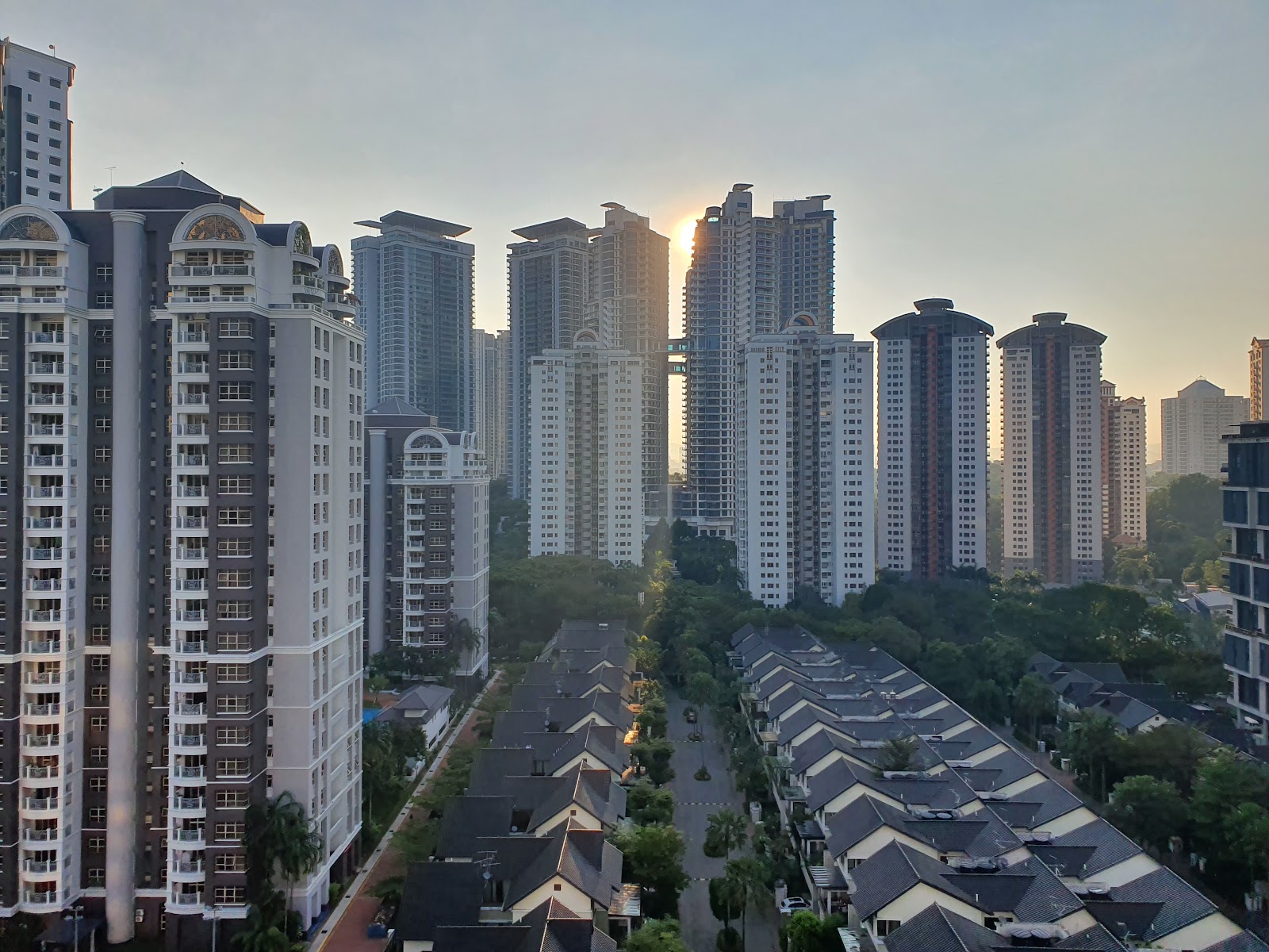 Ceriaan Kiara: Aerial view of a dense high-rise residential skyline at sunrise with landed housing rooftops in the foreground