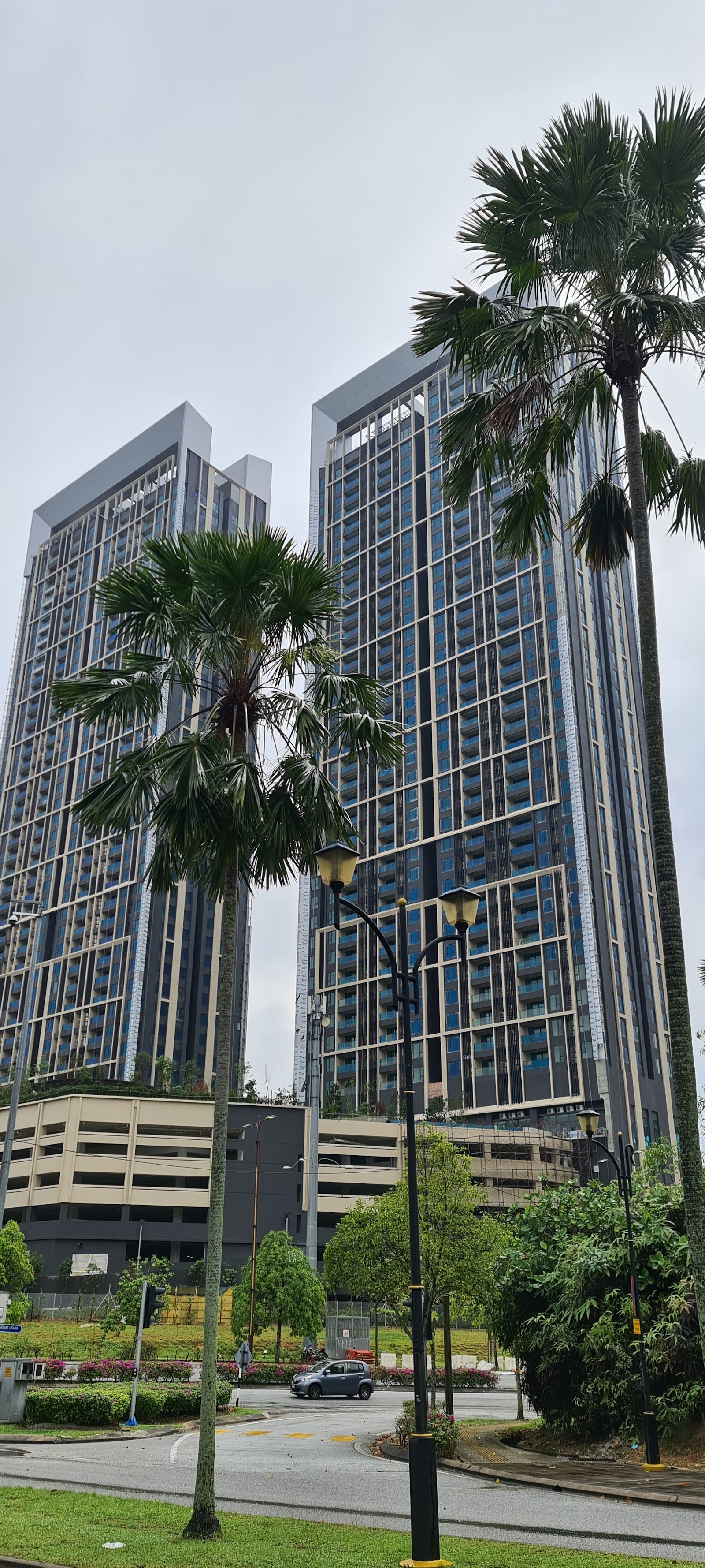 Residensi Solaris Parq: Twin high-rise residential towers viewed from ground level with palm trees, street lamps, and a parking garage in front