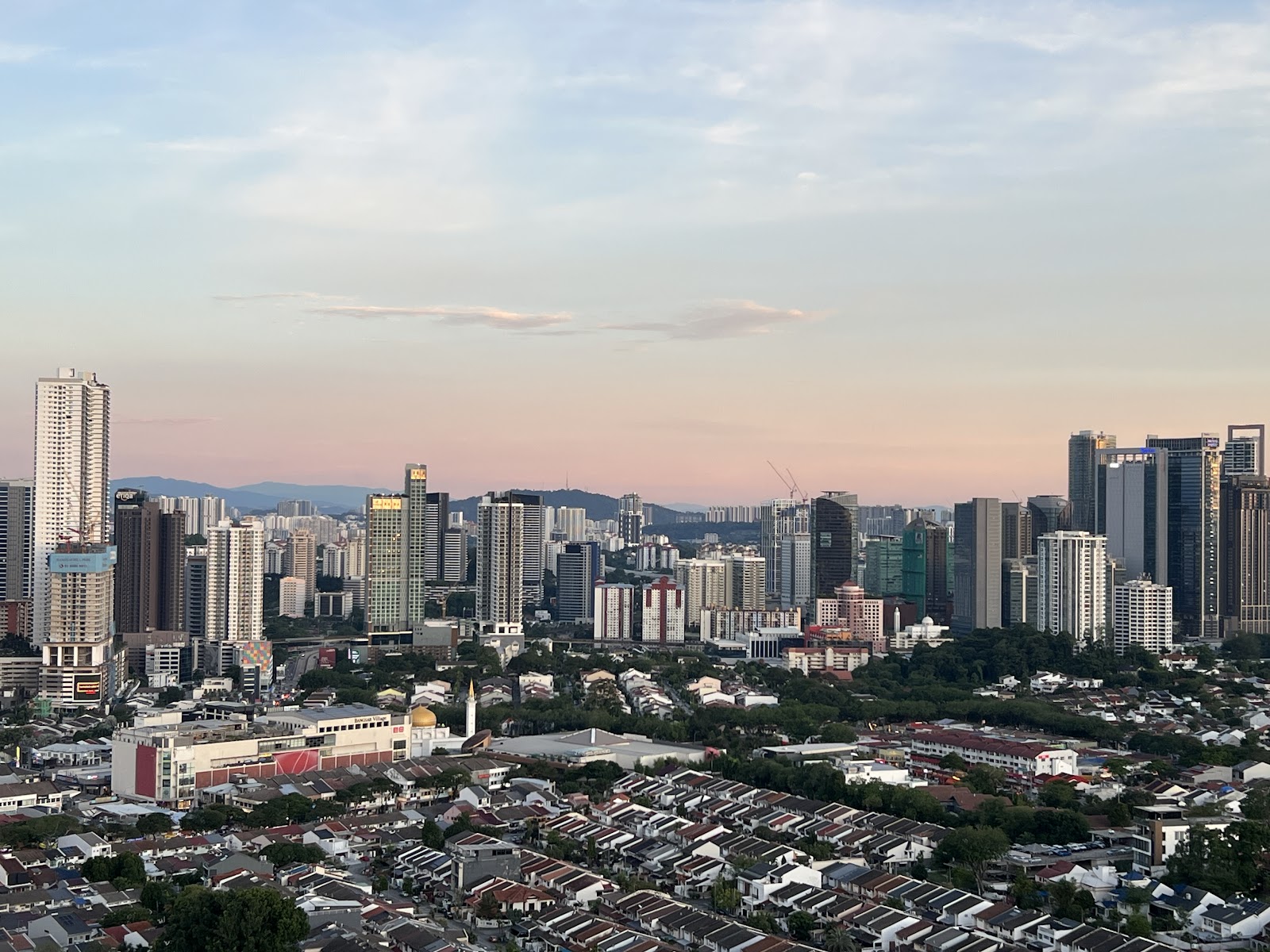 Sri Wangsaria: Aerial view of a city skyline with high-rise towers and low-rise housing at sunset, seen from a high vantage point