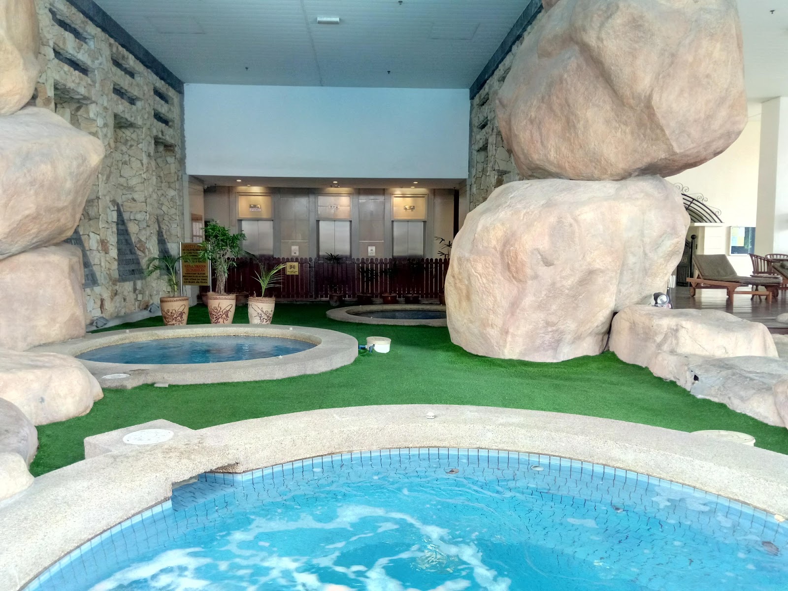Windsor Tower: Indoor spa/pool area with decorative rock formations, artificial turf, small jacuzzi pools, and elevator doors in the background