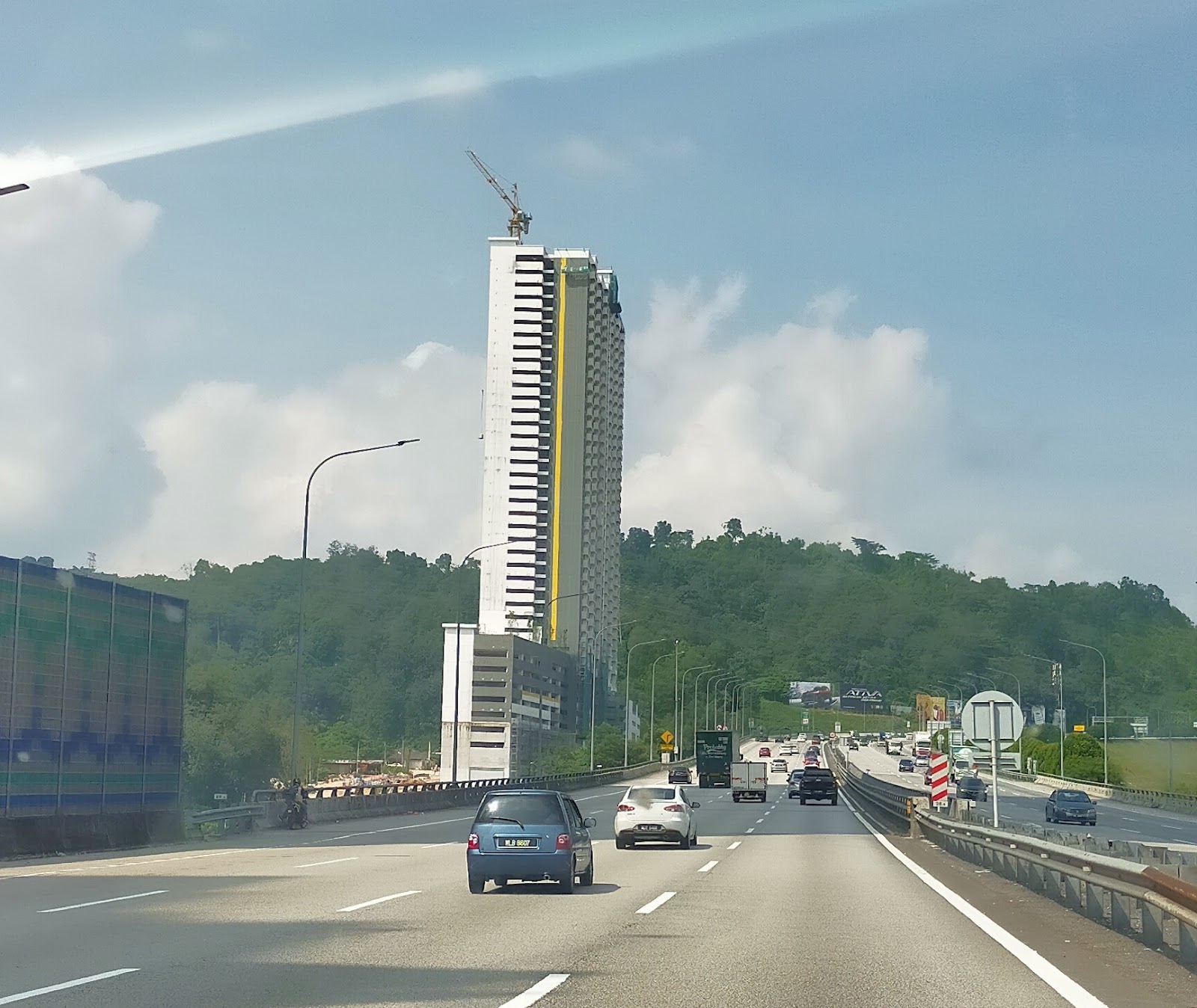 Kiara Kasih: A tall high-rise residential tower under construction, viewed from a highway with cars and greenery in the foreground