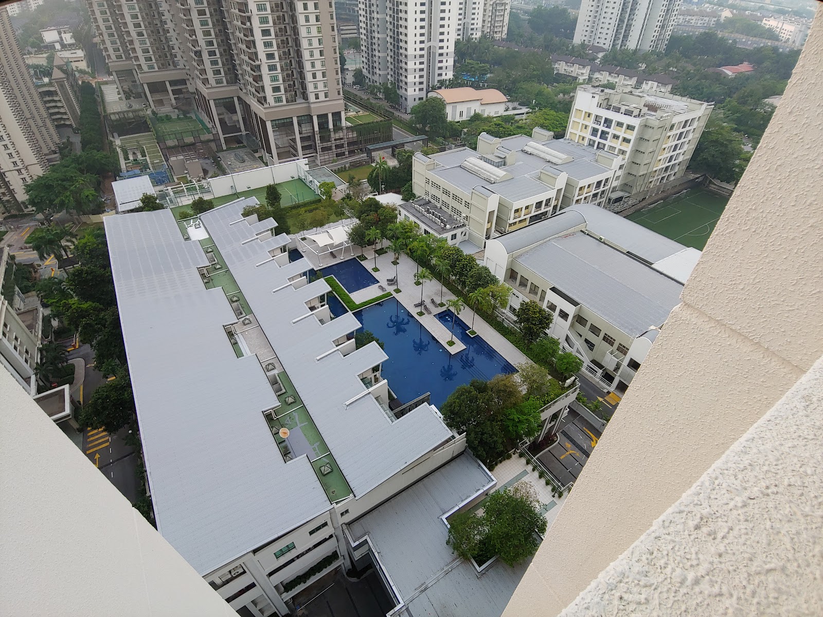 Kiara Designer Suites: Aerial view of a residential development's rooftop swimming pool, sun loungers, gardens and surrounding buildings, seen from a high floor balcony