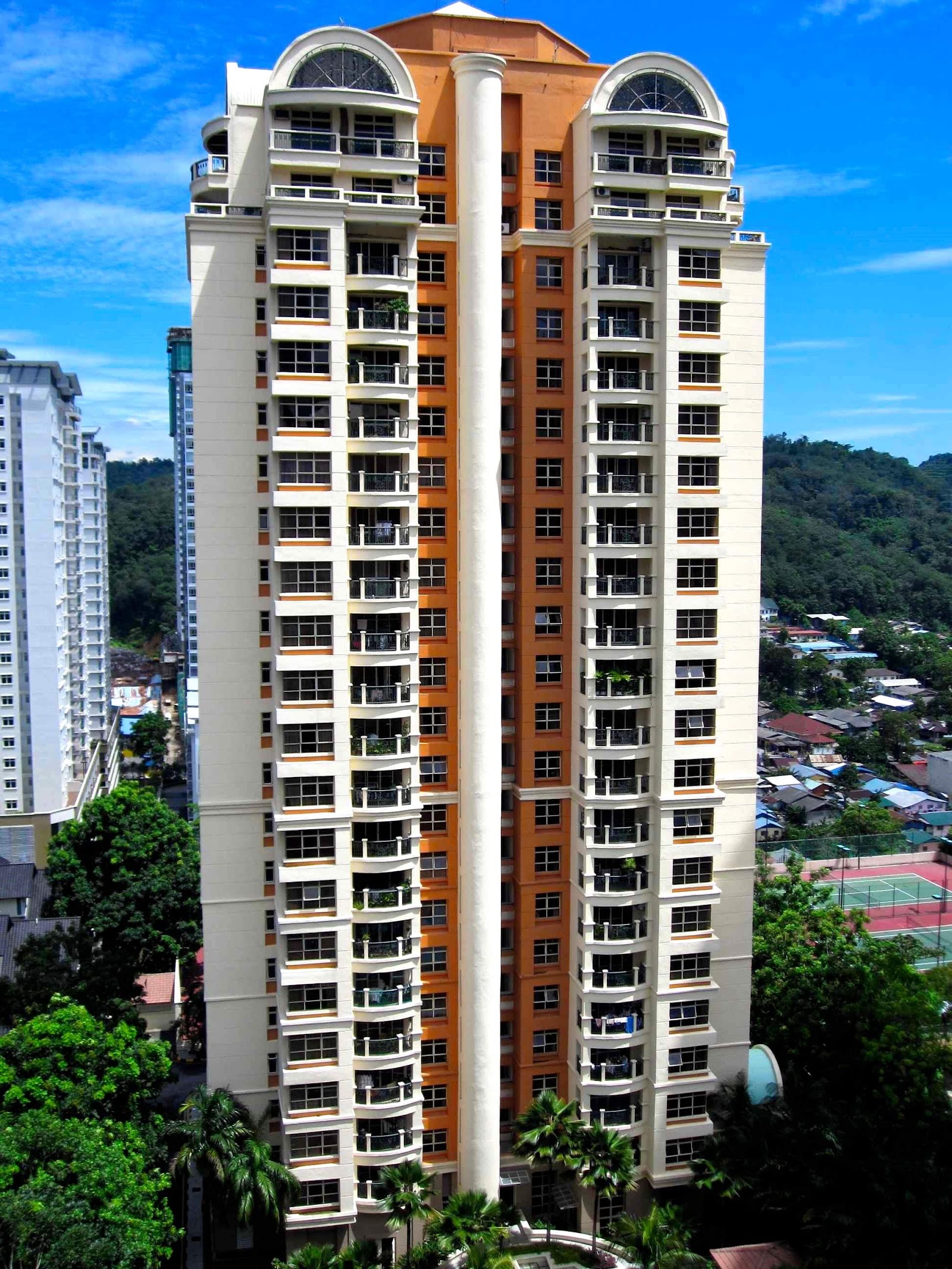 Almaspuri: A tall high-rise apartment tower with cream and orange facade, balconies, and twin domed rooftop features, surrounded by trees and other buildings