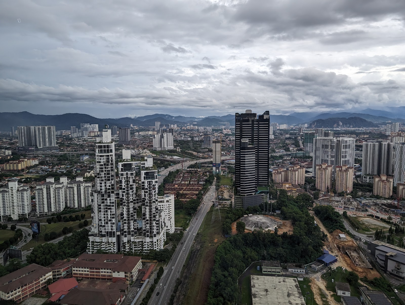 Icon Residence: Aerial cityscape view from a high-rise development showing surrounding towers, buildings, greenery and mountains under a cloudy sky