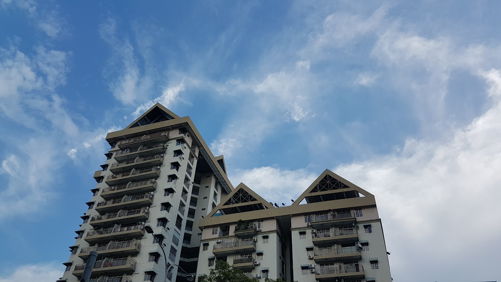 Fajaria Condominium: Low-angle view of a high-rise residential condominium tower with distinctive pyramid-shaped roof peaks against a blue sky with clouds
