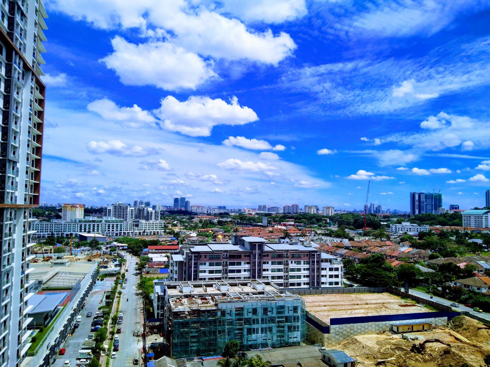 Pangsapuri Pelangi Ara: Aerial cityscape view from a high floor showing surrounding buildings, roads, and skyline under a blue sky with clouds