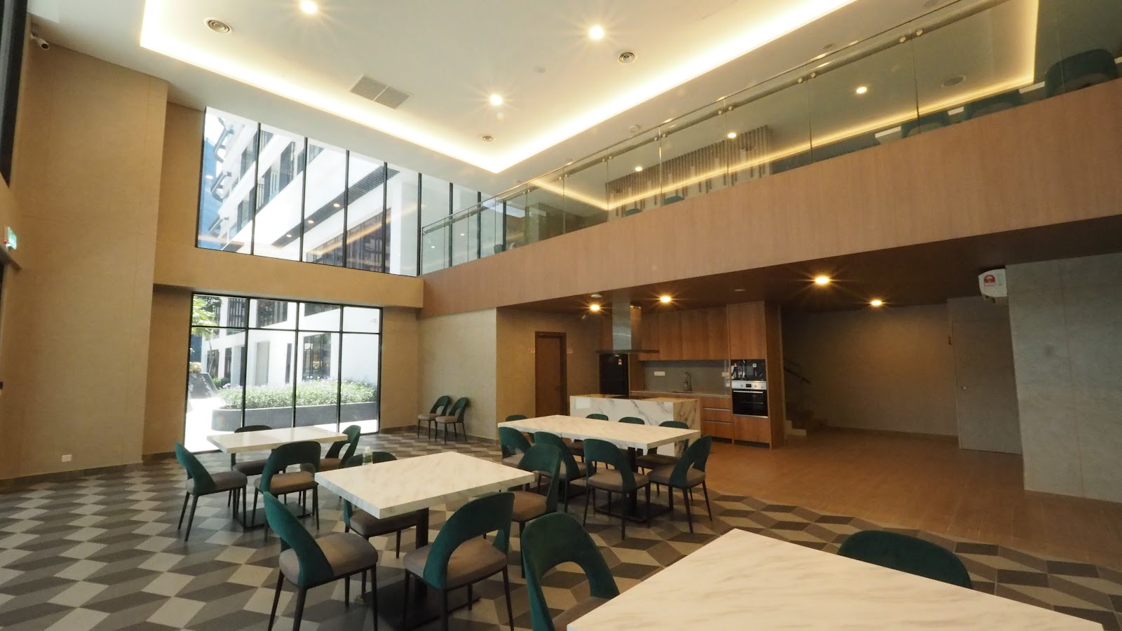Bangsar Hill Park: A shared dining/function lounge area with multiple marble tables and green chairs, an open kitchen counter, and a mezzanine level above, with large windows looking out to another building