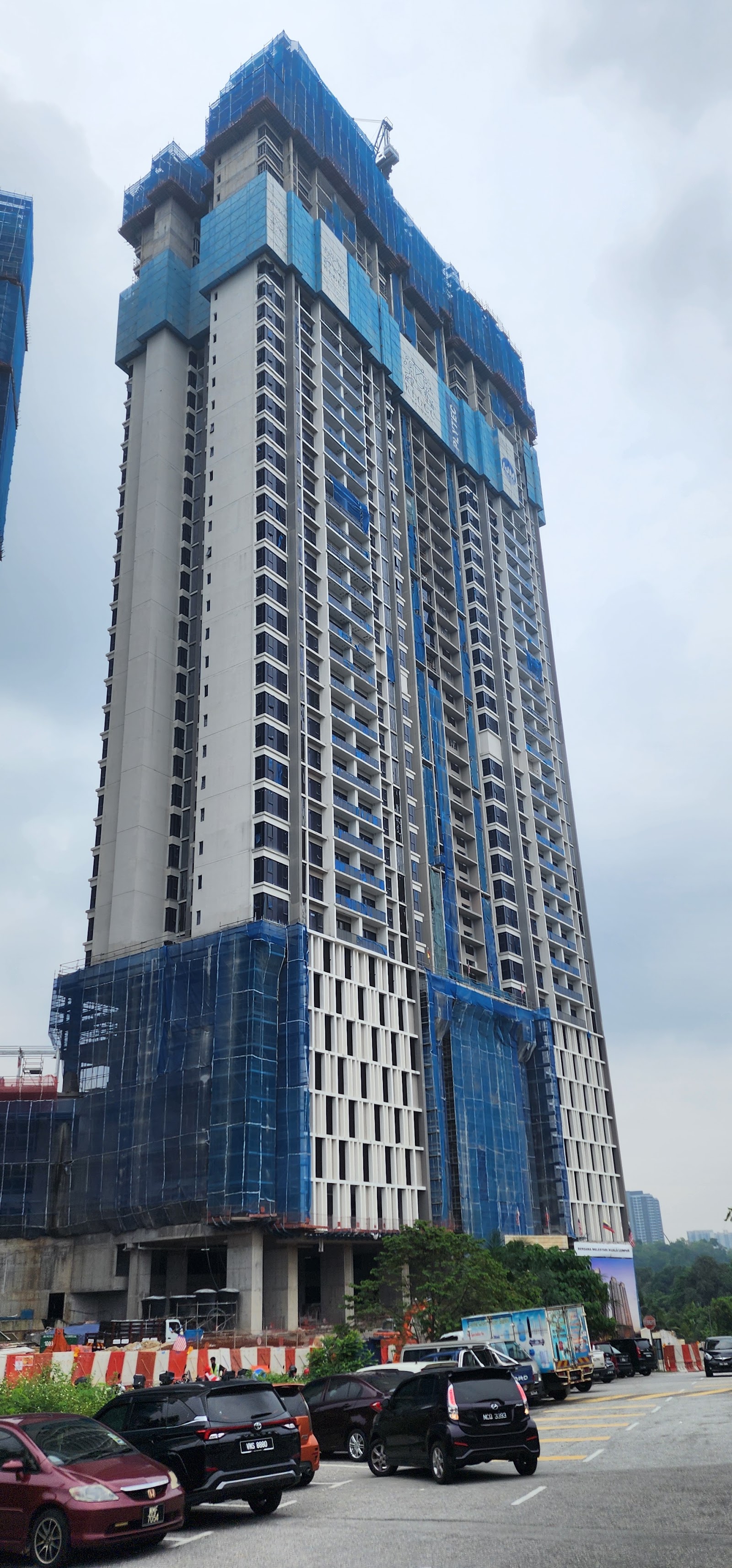 Jendela Residences: A high-rise residential tower under construction, with blue safety netting and scaffolding on lower floors, cars parked in front