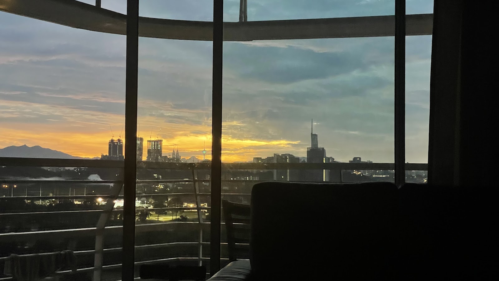 The Plaza Condominium: City skyline at sunset viewed through a window, with a couch silhouette in the foreground