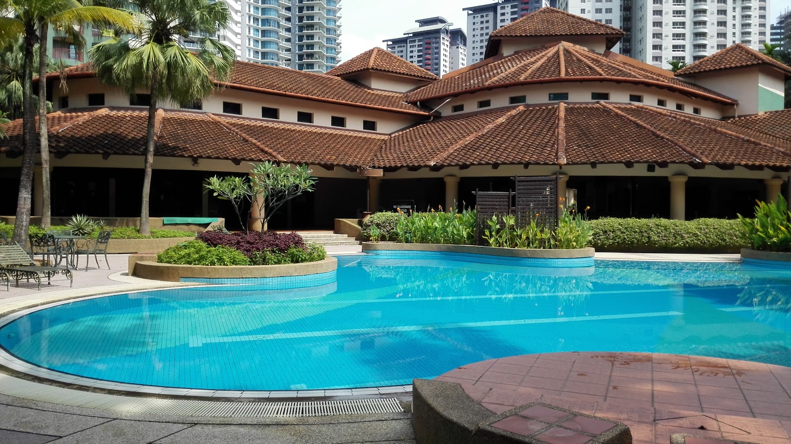 Mont Kiara Sophia: An outdoor swimming pool surrounded by landscaped gardens and a traditional-roofed pavilion building, with high-rise towers in the background