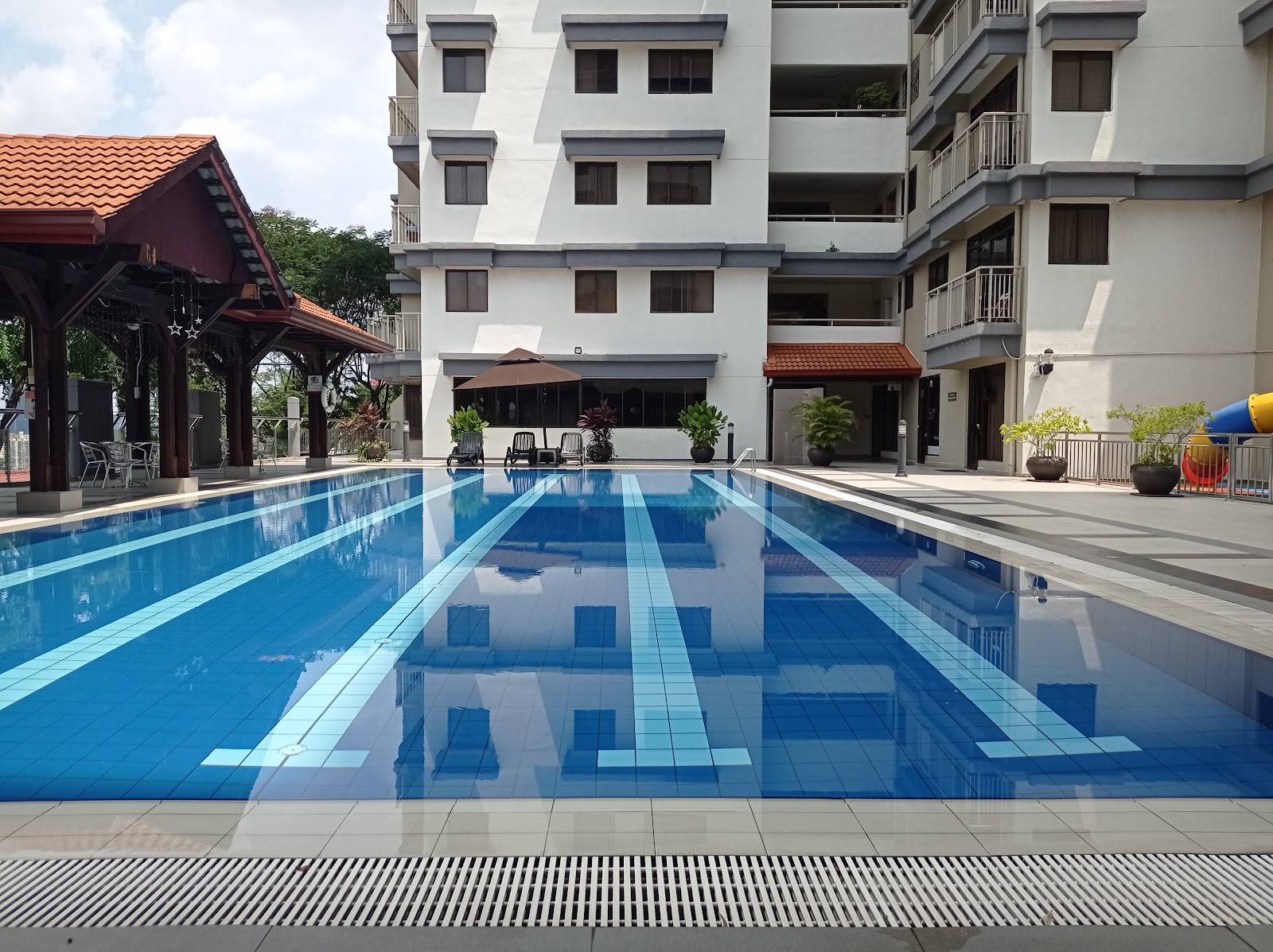 Cascadium: Outdoor swimming pool with lane markers next to a residential building, with lounge chairs, a pavilion, and a playground slide visible