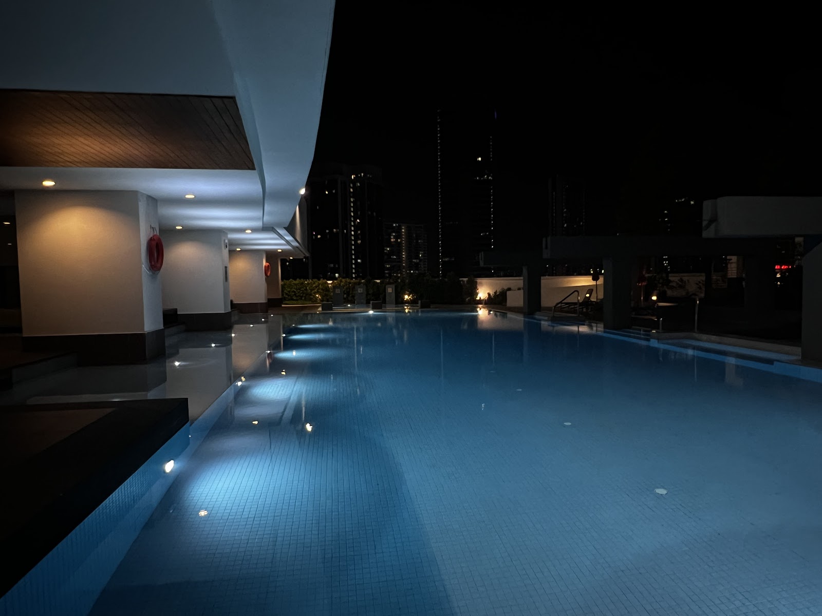 Sinaran TTDI: Nighttime rooftop swimming pool with underwater lighting and a city skyline in the background