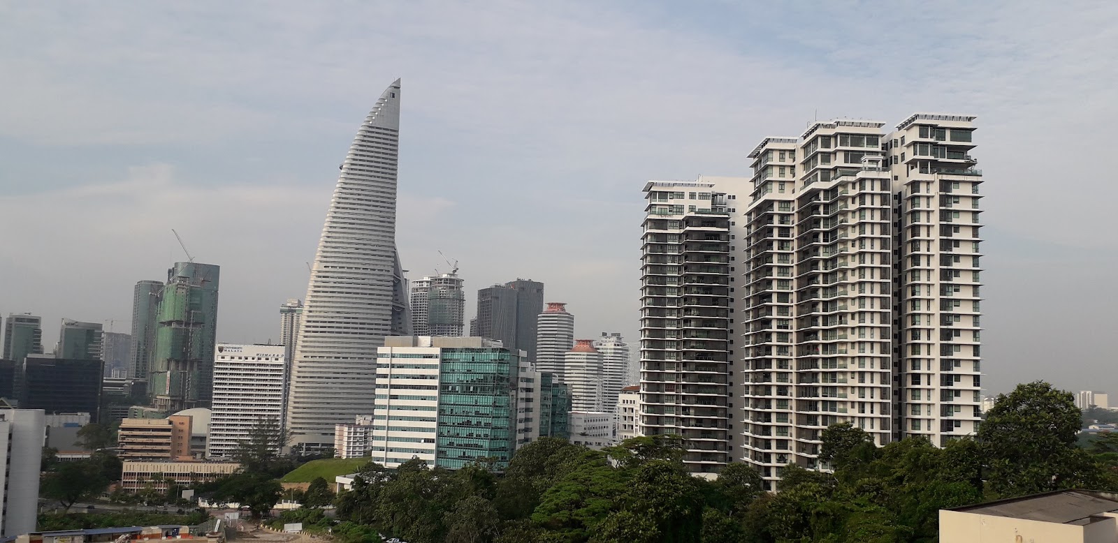 Pantai Towers: Skyline view of city skyscrapers including a distinctive twisted tower and residential high-rise buildings surrounded by trees