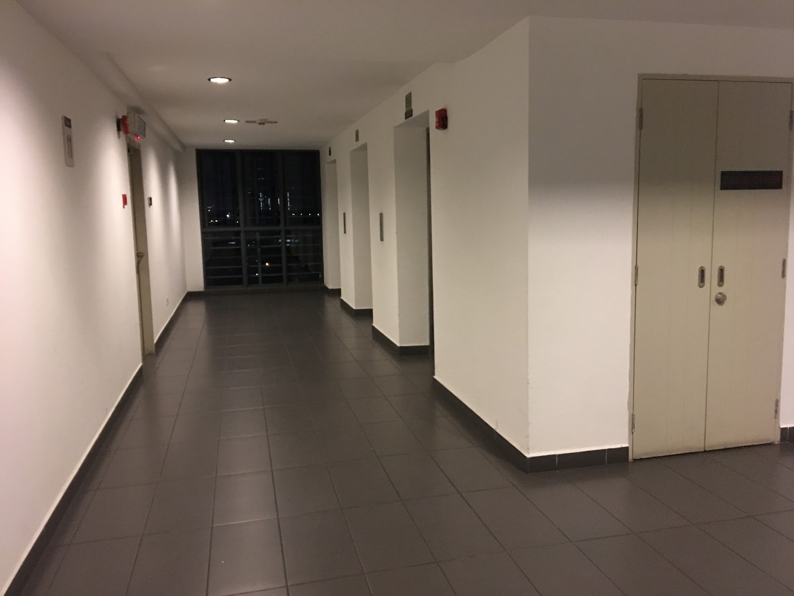 Boulevard Residence: Interior hallway of a residential building with tiled floor, unit doors, and windows showing city lights at night