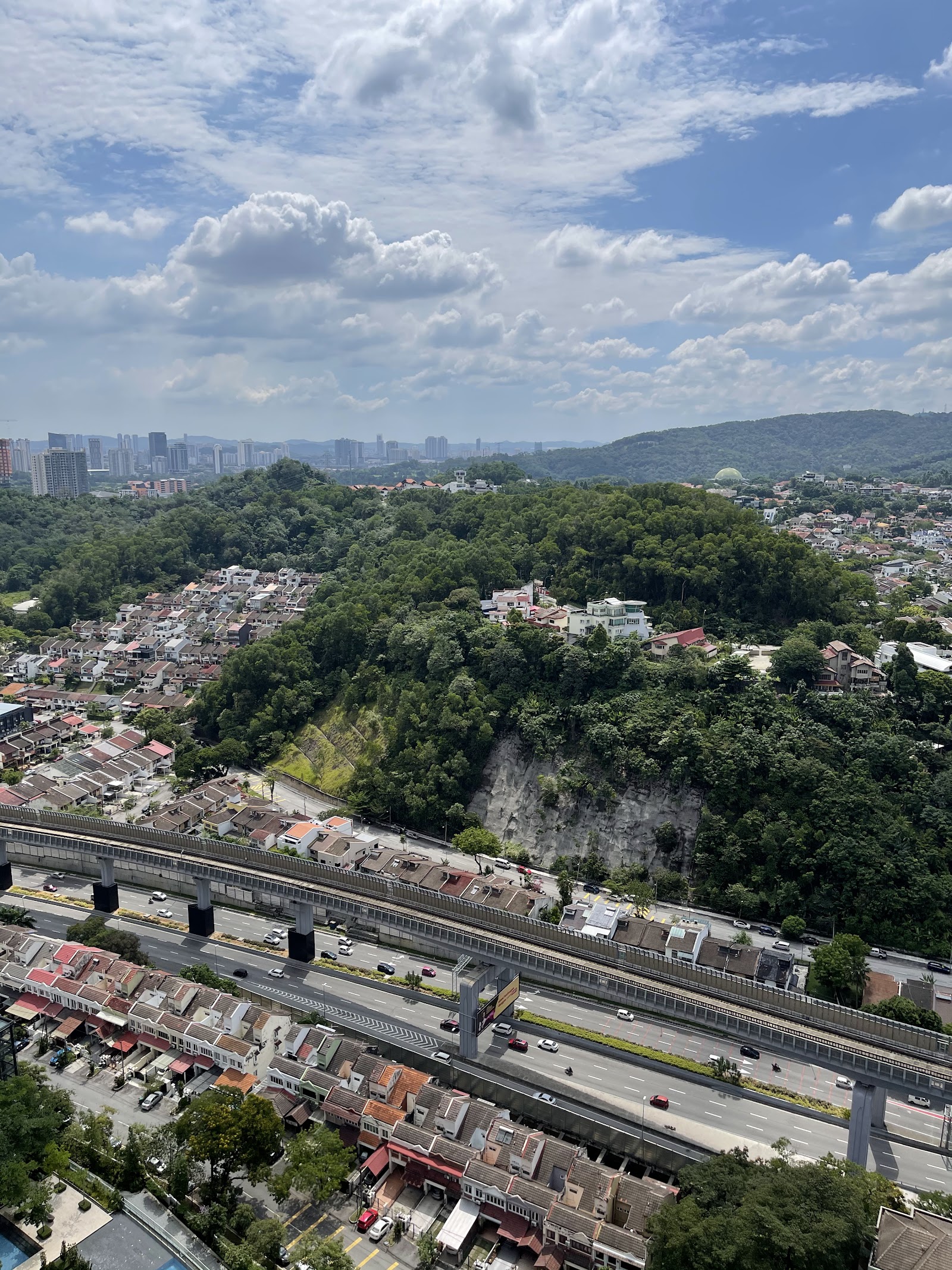 Serai: Aerial view from a high-rise development overlooking a hillside residential area, highway, and city skyline in the distance
