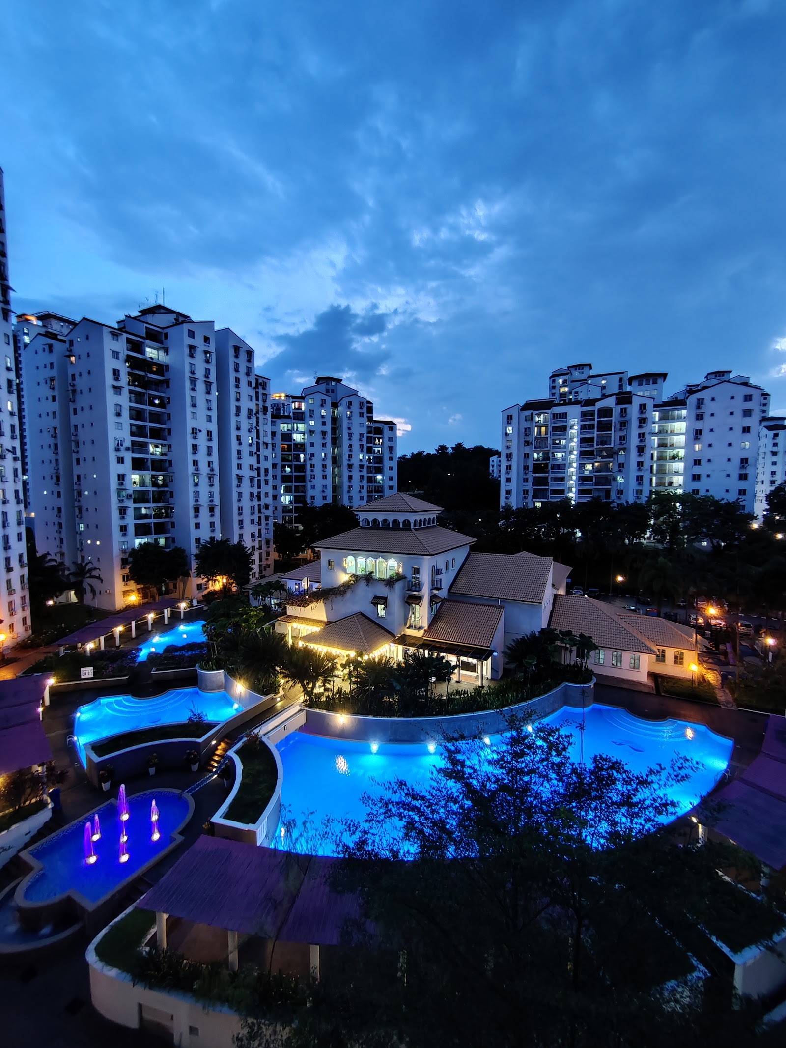 Pantai Hillpark 2: Nighttime view of a resort-style swimming pool with fountains, illuminated in blue, surrounded by high-rise apartment towers and a clubhouse building