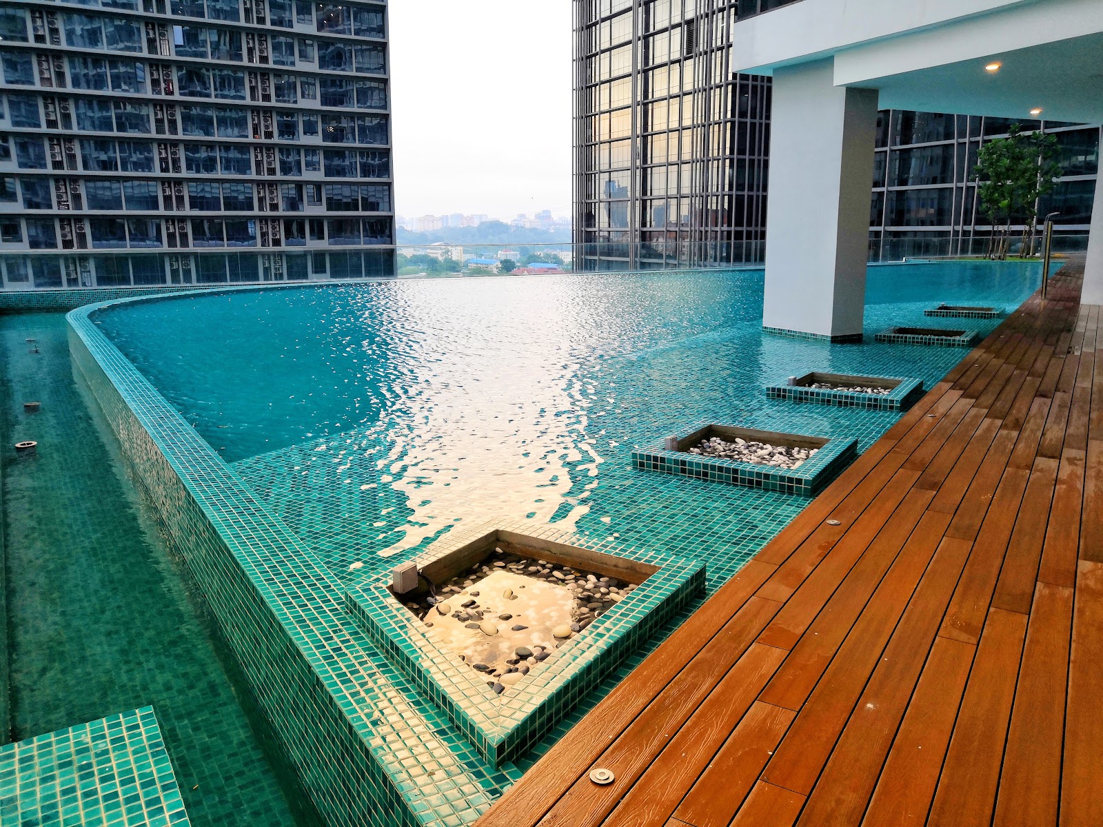 KL Gateway, Premium Residences: Rooftop infinity-edge swimming pool with teal mosaic tiles, wooden deck, and planter boxes, surrounded by high-rise towers