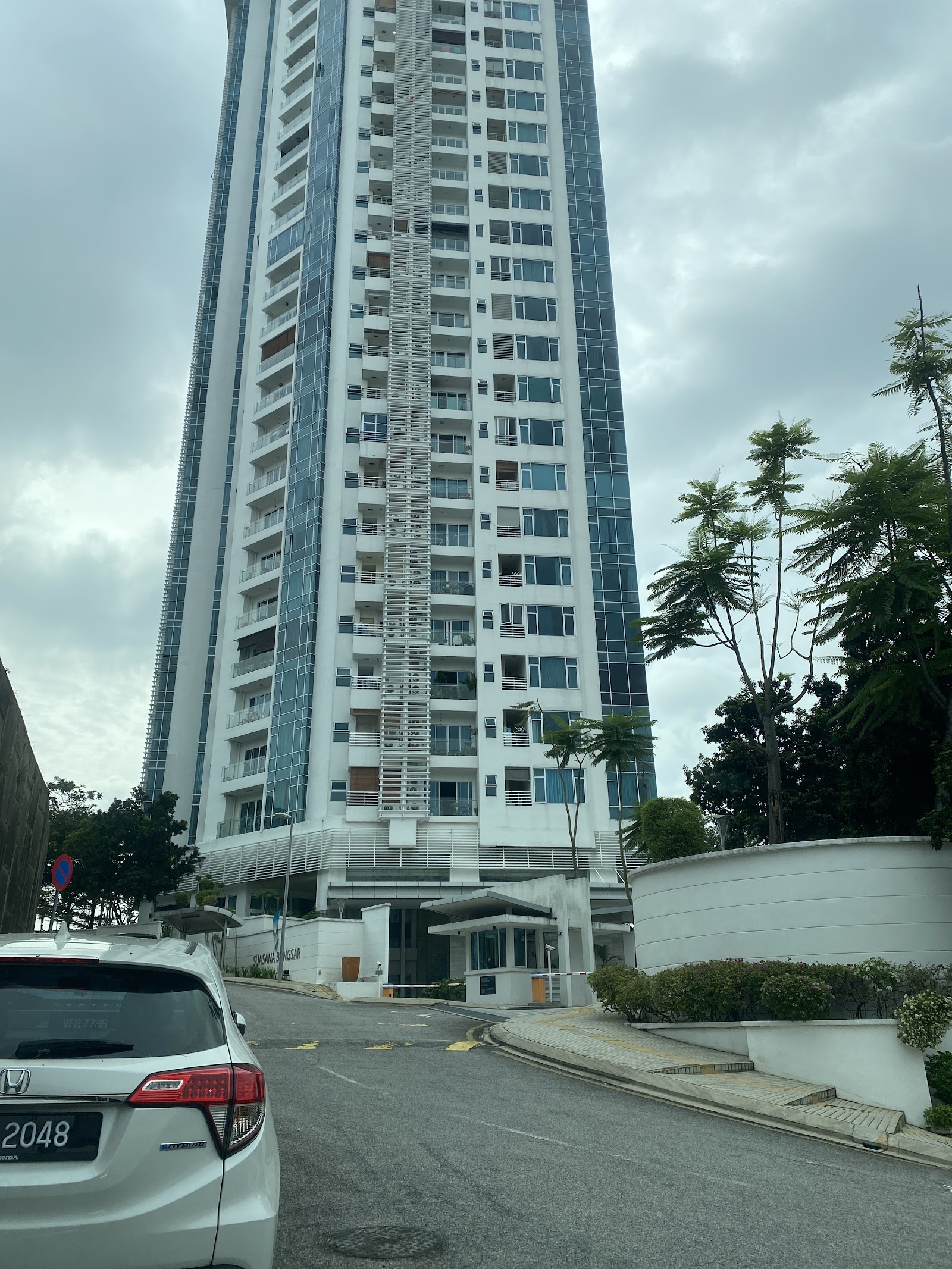 Suasana Bangsar: Tall residential tower with glass and white facade, seen from street level with a parked car in foreground