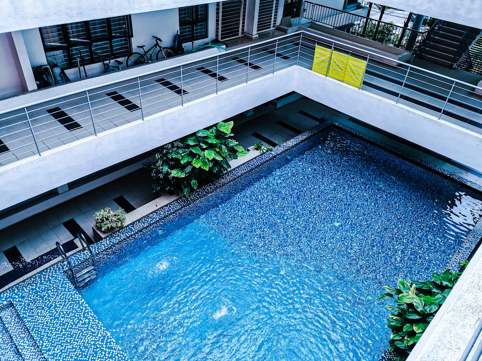 Laman Ara Utama: Aerial view of a swimming pool in a residential courtyard, surrounded by balconies with railings, bicycles, and greenery