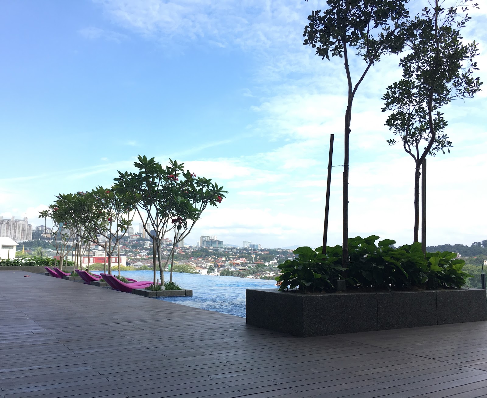 Nadi Bangsar: Rooftop infinity pool deck with sun loungers, potted trees and city skyline view
