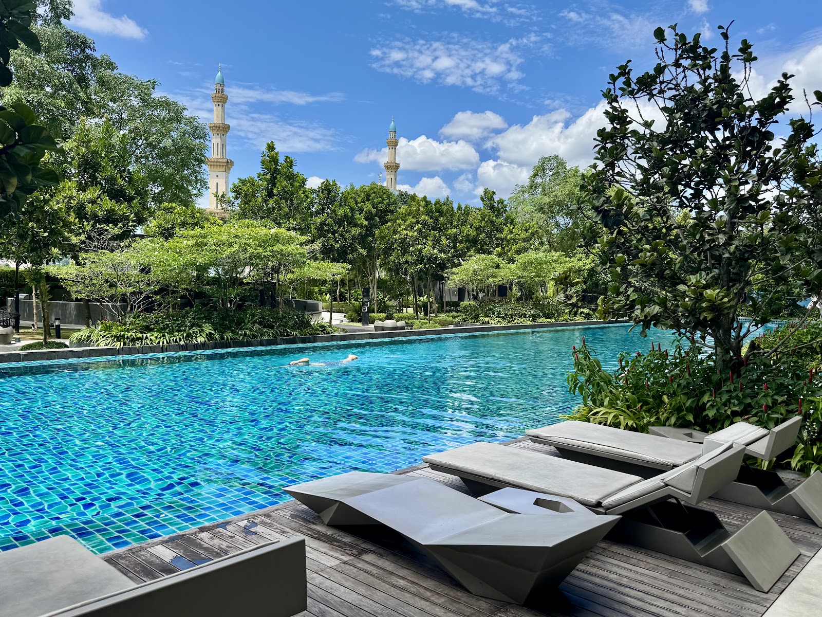 Residensi Solaris Parq: Swimming pool with lounge chairs on a wooden deck, surrounded by trees and mosque minarets visible in the background