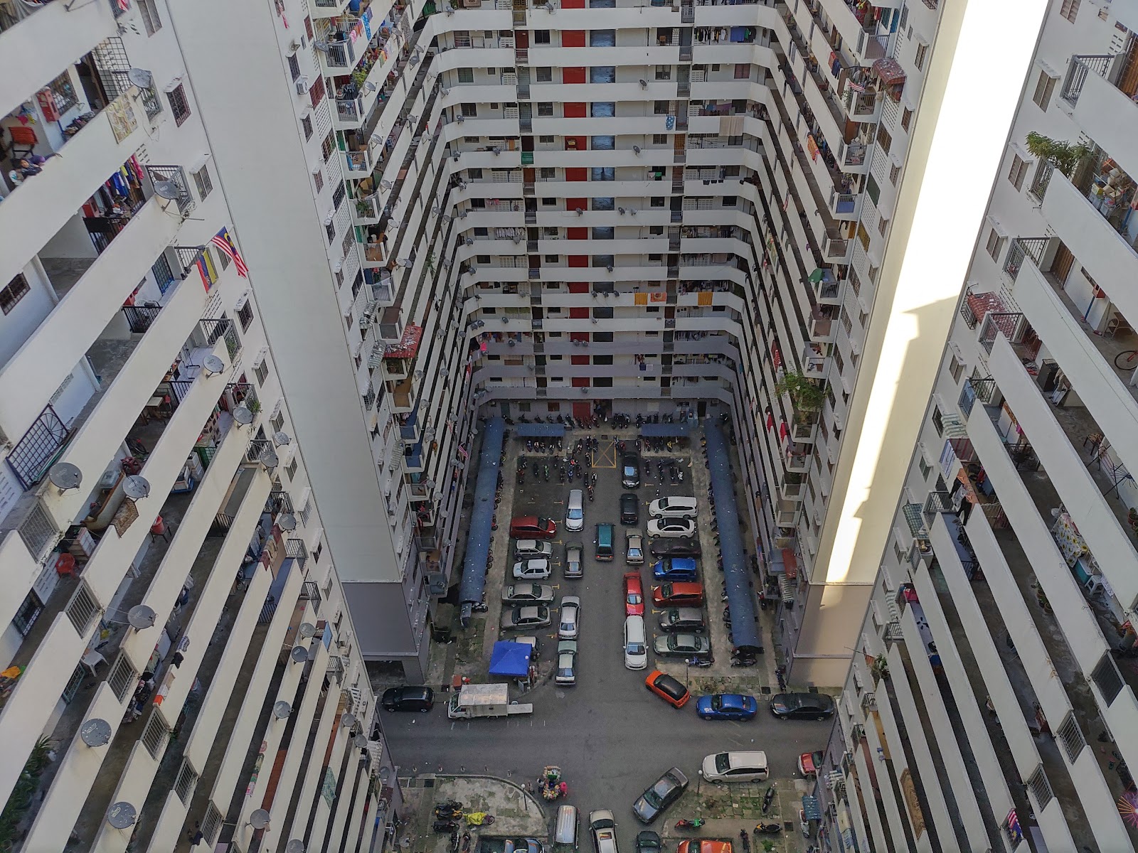 Putra Ria Apartment: Aerial view down into the courtyard of a high-rise residential apartment block, showing many floors of balconies surrounding a parking lot filled with cars