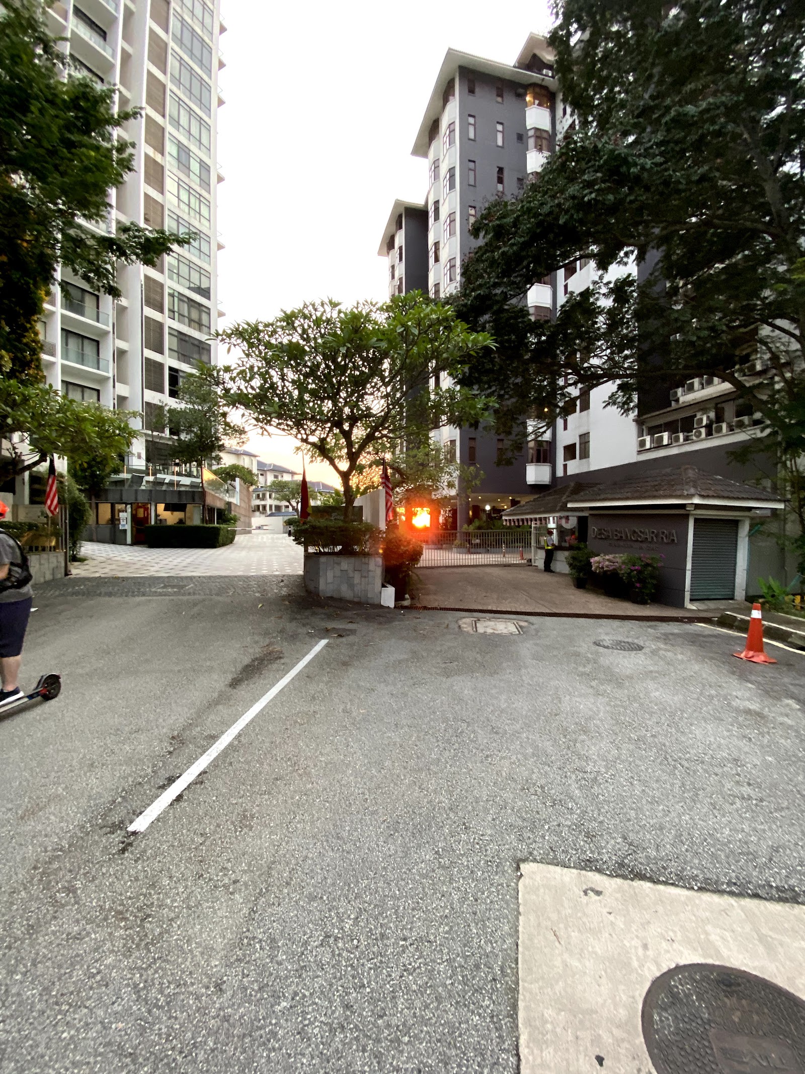 Desa Bangsar Ria: Street view of a residential condominium entrance with gated driveway, guard house, flags, and high-rise towers in the background
