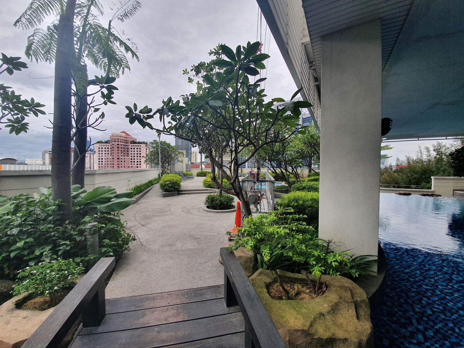 Suasana Bangsar: Rooftop garden walkway with pool area alongside, surrounded by tropical plants and city skyline view
