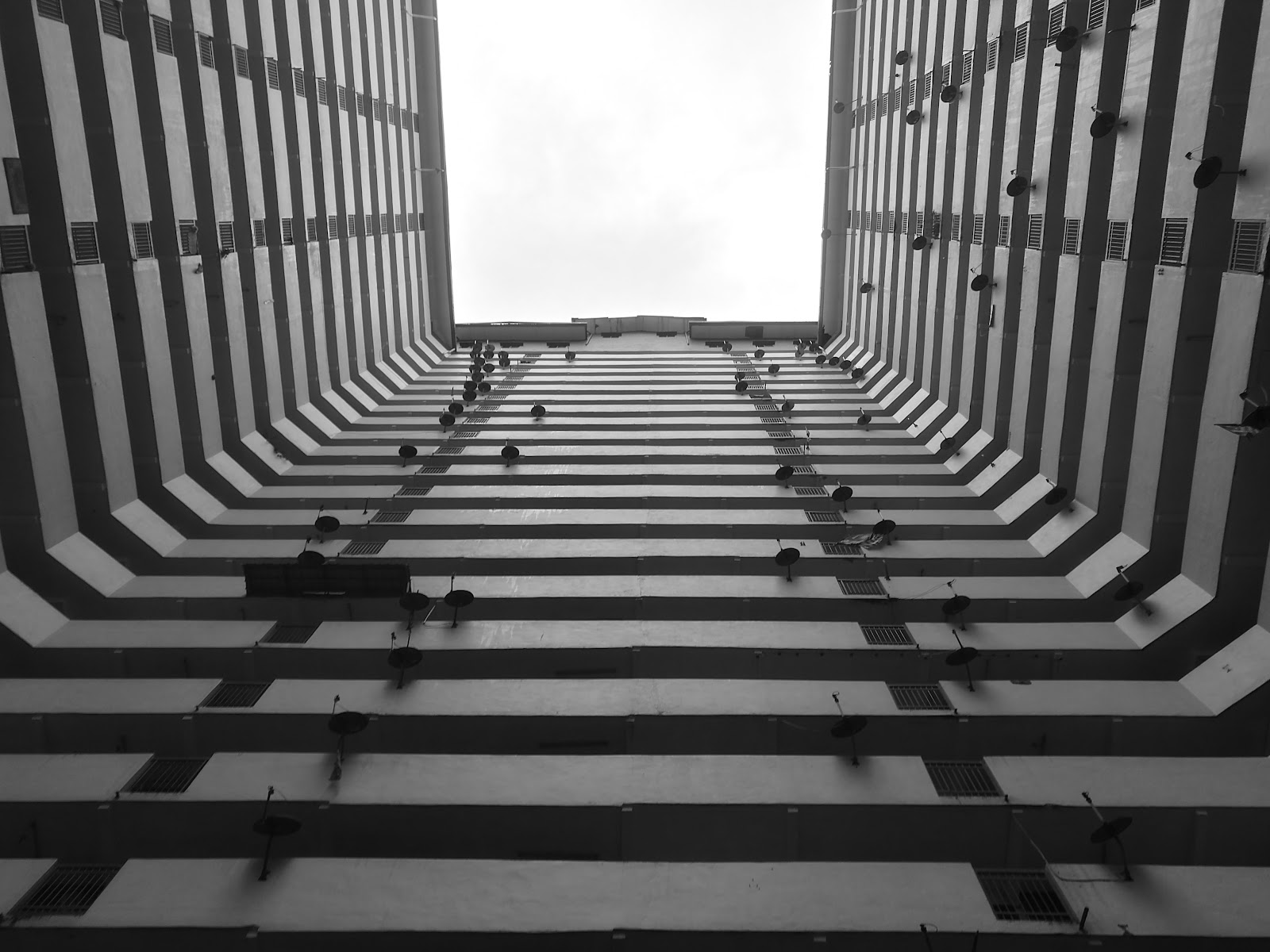 Putra Ria Apartment: Upward view of a building's inner courtyard facade, showing symmetrical rows of windows and satellite dishes converging toward the sky