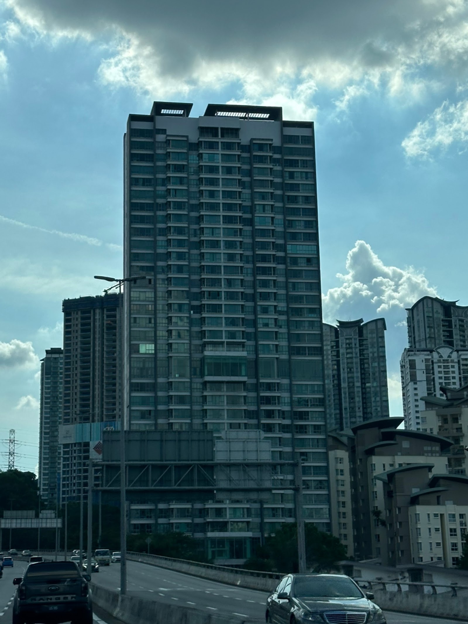 Gateway Kiaramas: A tall glass residential skyscraper photographed from a roadway with cars in the foreground and other high-rise buildings in the background.