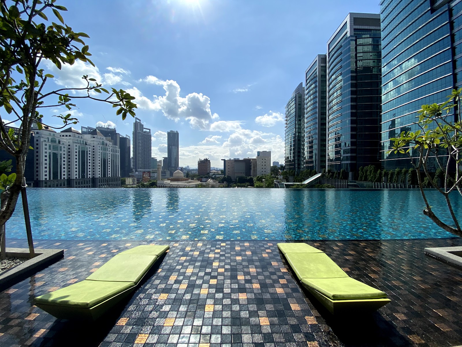 Novum: Rooftop infinity pool with lounge chairs overlooking a city skyline of high-rise buildings