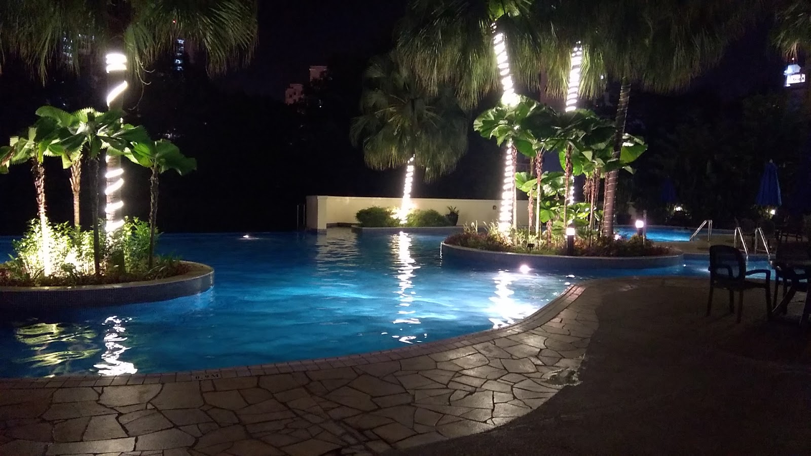 La Grande Kiara: Nighttime swimming pool with palm trees illuminated by vertical lights and poolside seating area
