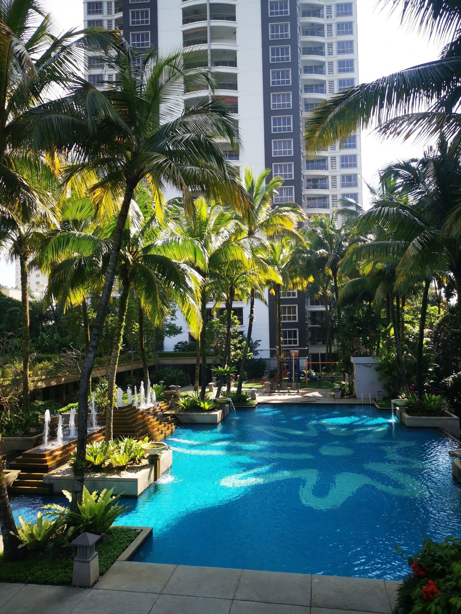 Kiaramas Cendana: Swimming pool with fountains surrounded by palm trees, with a high-rise residential tower in the background