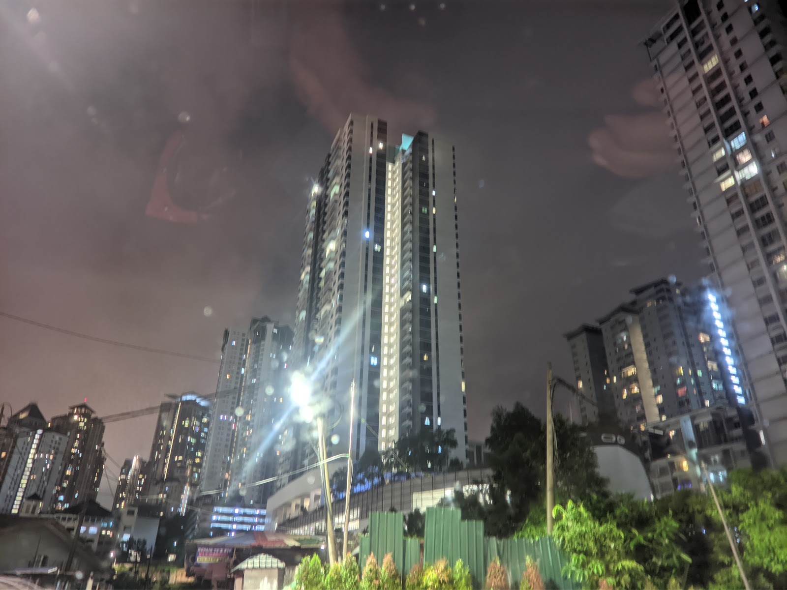 Residensi Sefina Mont Kiara: Night view of high-rise residential towers with illuminated windows, seen from outside with trees and greenery in foreground
