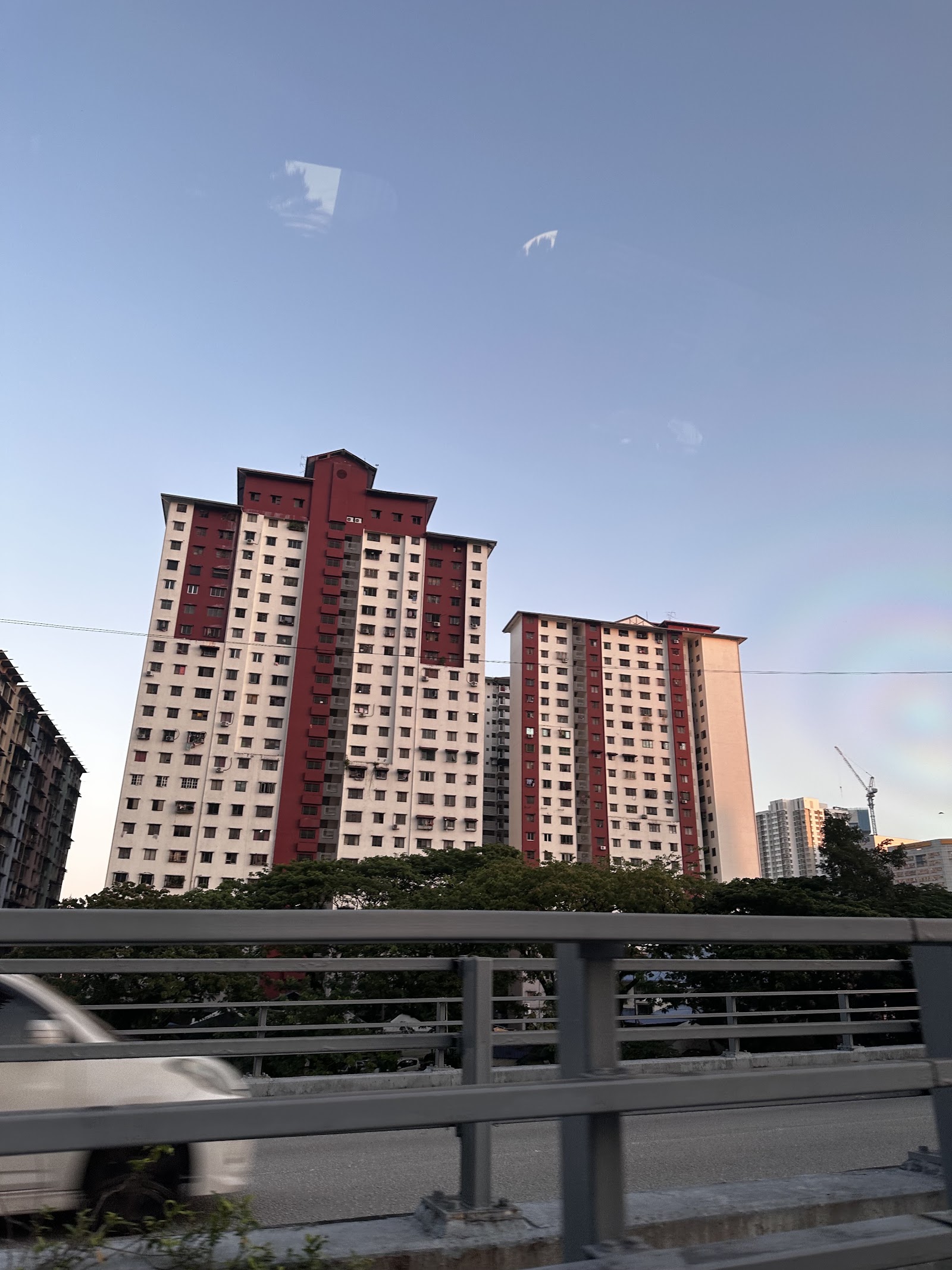 Putra Ria Apartment: View of tall red and white residential apartment towers seen from a road with a guardrail in the foreground