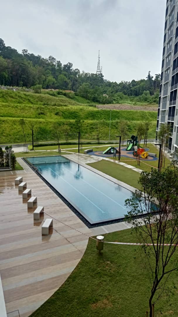 Suria Pantai Residency: Swimming pool, sun deck, and children's playground within the residential development grounds, with hills in the background