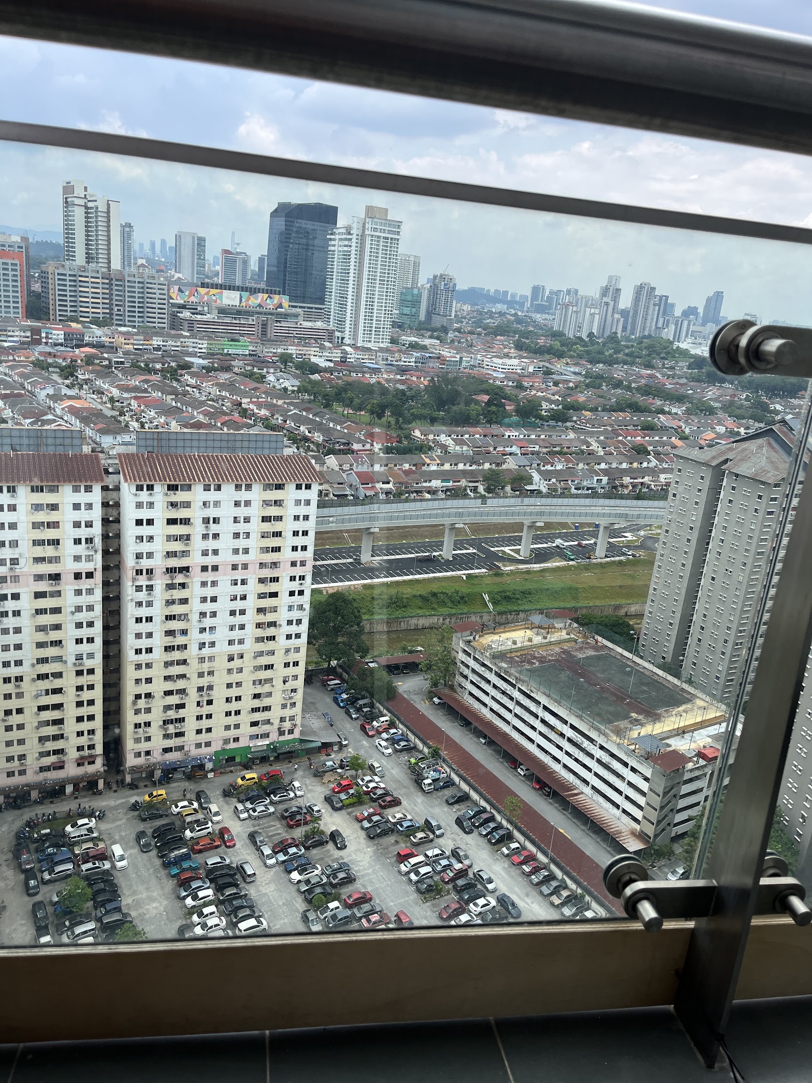 Glomac Centro: View from a high-rise balcony overlooking a residential neighborhood, parking lots, an elevated roadway, and distant city skyline