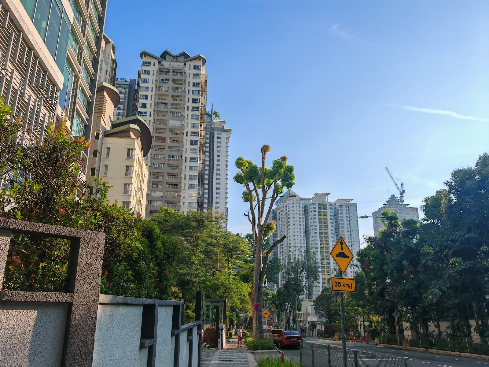 Gateway Kiaramas: Street view outside residential towers with trees, a speed limit sign, and construction crane in the background
