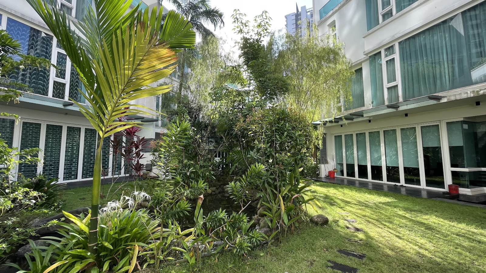 Kiara 9 Residency: A landscaped garden courtyard with lush tropical plants and a water feature between two wings of a residential building