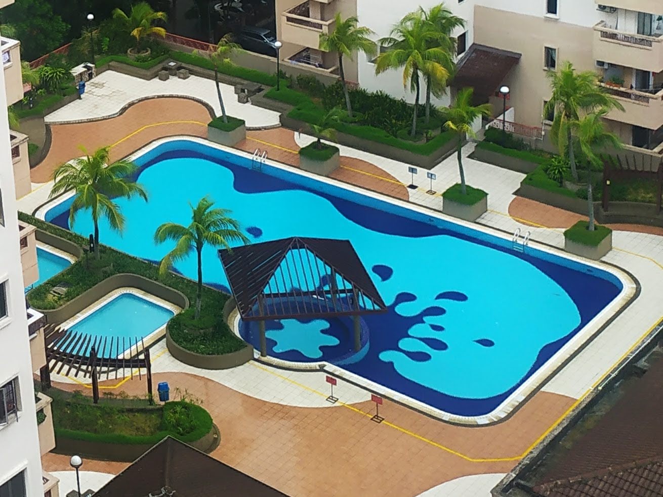 Pelangi Damansara: Aerial view of a large swimming pool complex with palm trees, a gazebo, and surrounding buildings
