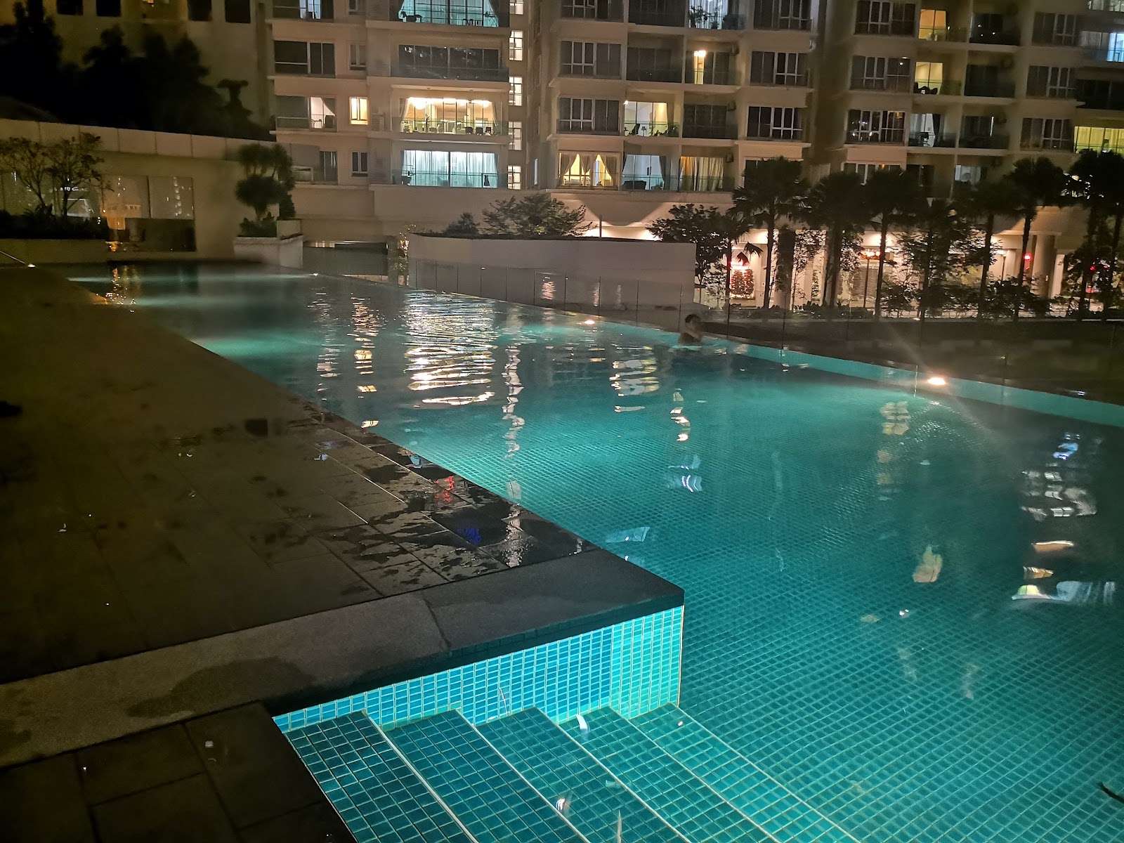 Camellia Serviced Suites: Nighttime infinity pool at a residential development with a swimmer, overlooking illuminated tower facades and landscaping
